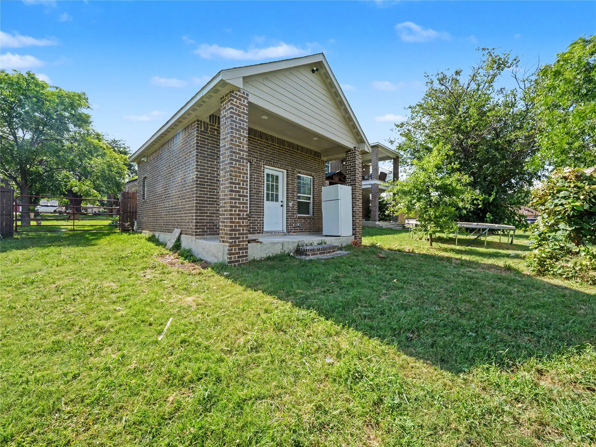 Brick exterior with white paneled door, covered patio, concrete slab foundation, and fenced perimeter