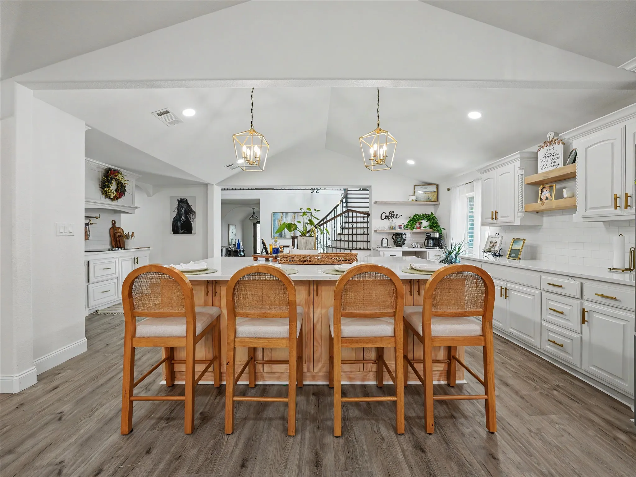 Kitchen featuring a central island with countertop seating, white cabinetry with gold-tone hardware, subway tile backsplash, wood-finish flooring, and vaulted ceiling with pendant lighting