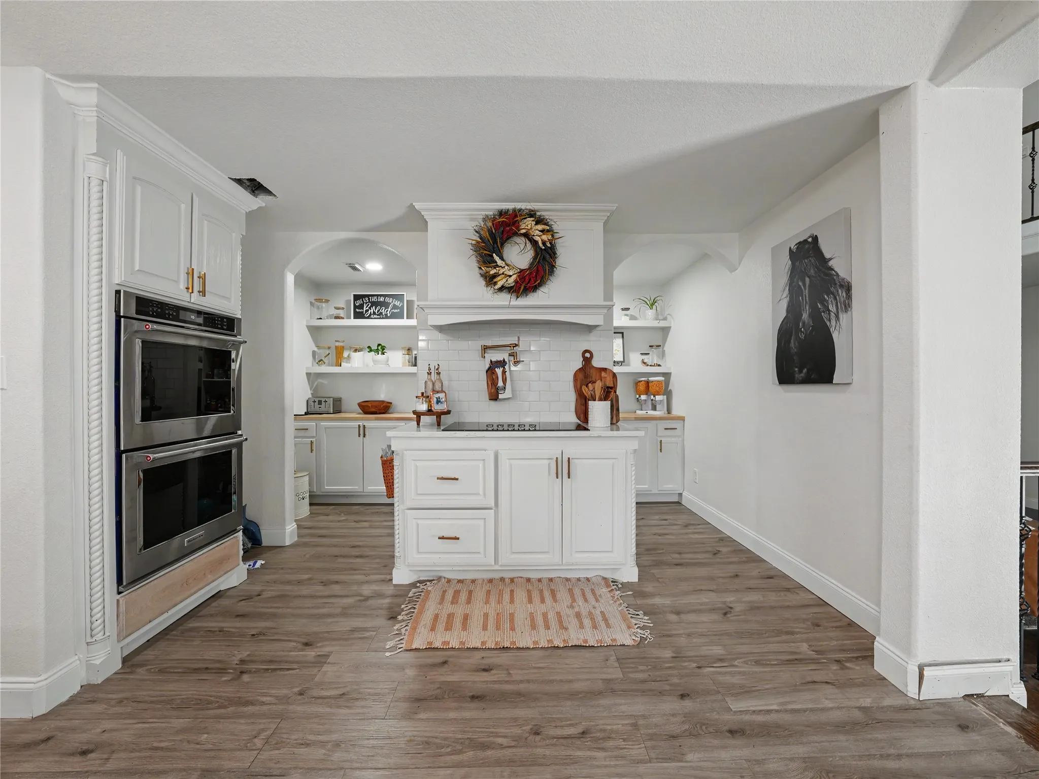 Kitchen featuring a central island, white cabinetry, wood-finish flooring, stainless steel double wall ovens, and open shelving