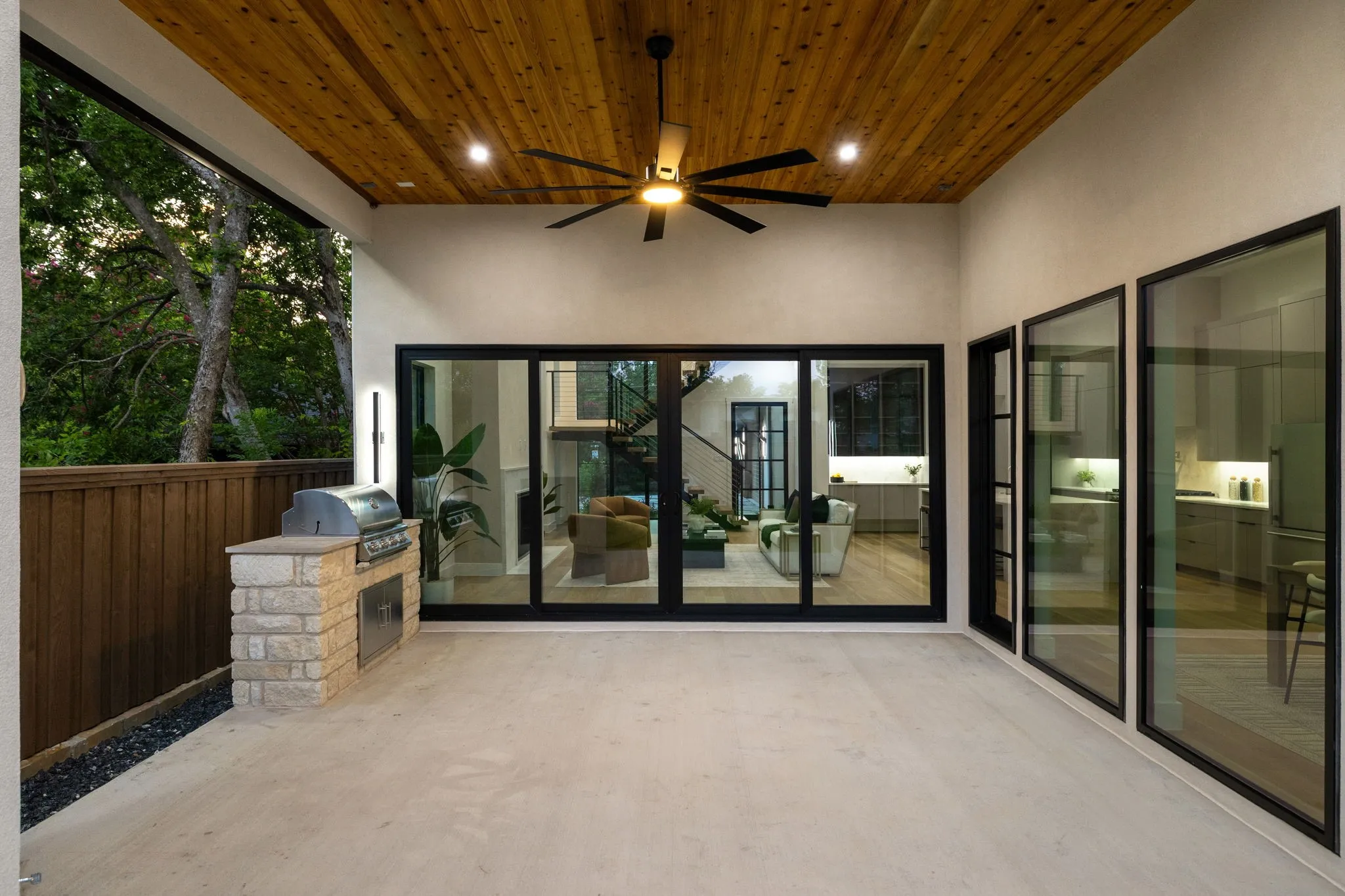 Expansive covered patio featuring a cedar plank ceiling with a ceiling fan, a built-in stone grill station, and a concrete floor