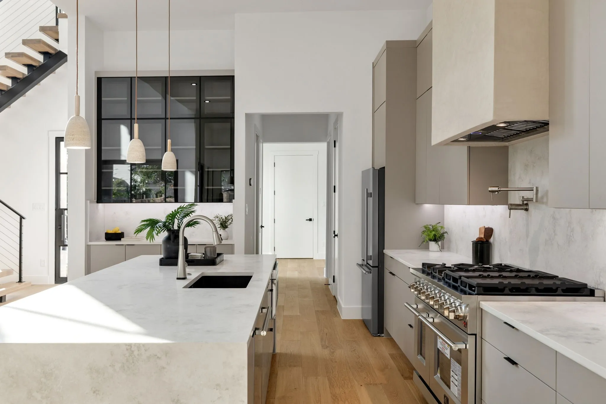 Gourmet kitchen featuring a substantial island with integrated sink, sleek pot filler faucet, professional-grade range, stainless steel French-door refrigerator, and floor-to-ceiling cabinetry with grid glass accents