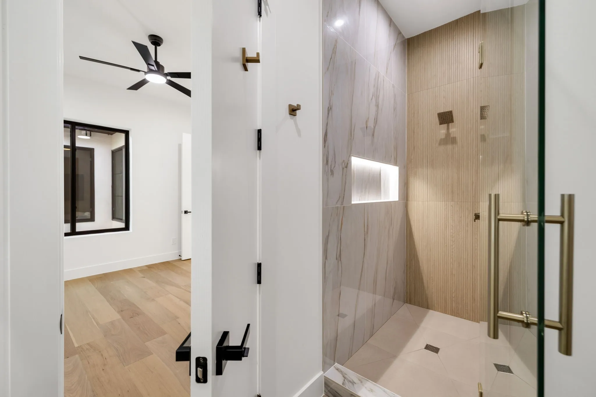 Walk-in shower featuring a glass enclosure with brass-finish hardware, tiled walls with an illuminated niche, and a contrasting tiled floor