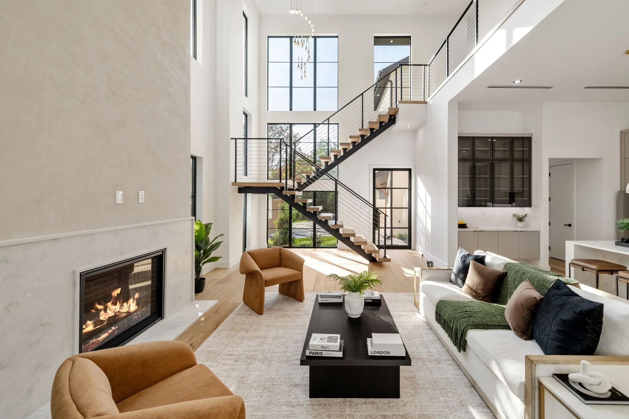Two-story living area featuring a prominent staircase with metal railings and open treads, a fireplace with a light-toned surround, expansive windows, wood-finish flooring, and a built-in wet bar with dark-framed cabinetry