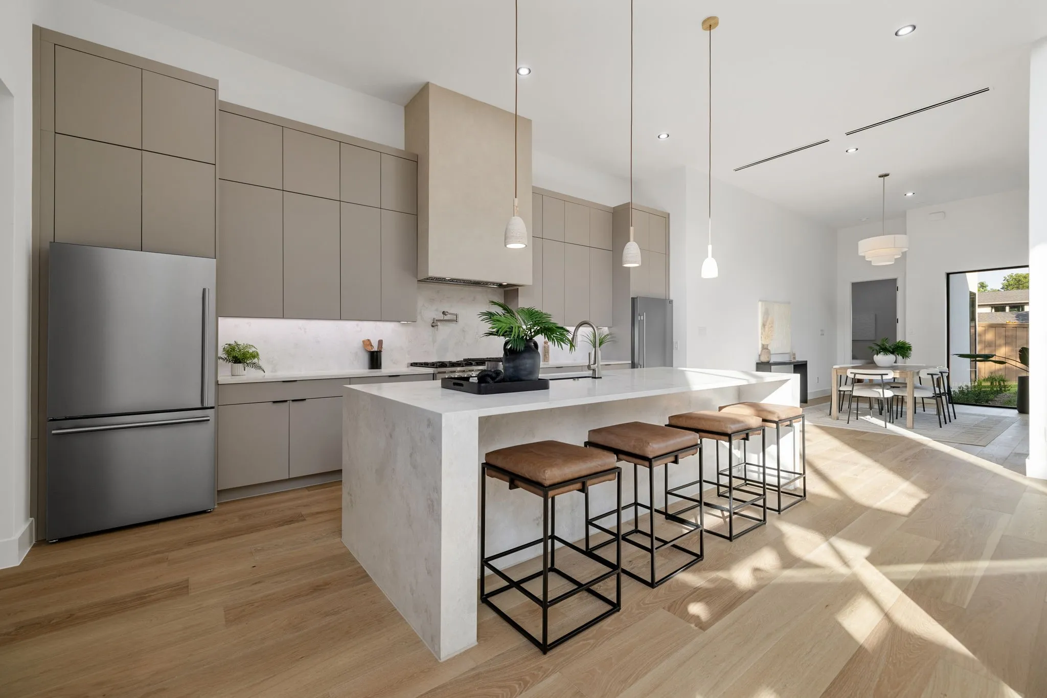 Modern kitchen featuring light wood-finish flooring, full-height cabinetry with integrated refrigerator, a large center island with waterfall countertop, and pendant lighting