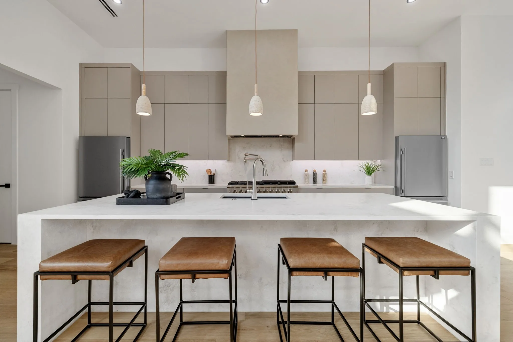 Modern kitchen featuring an extended island with waterfall countertop, integrated cooktop, ceiling-mounted range hood, stainless steel appliances, and minimalist cabinetry