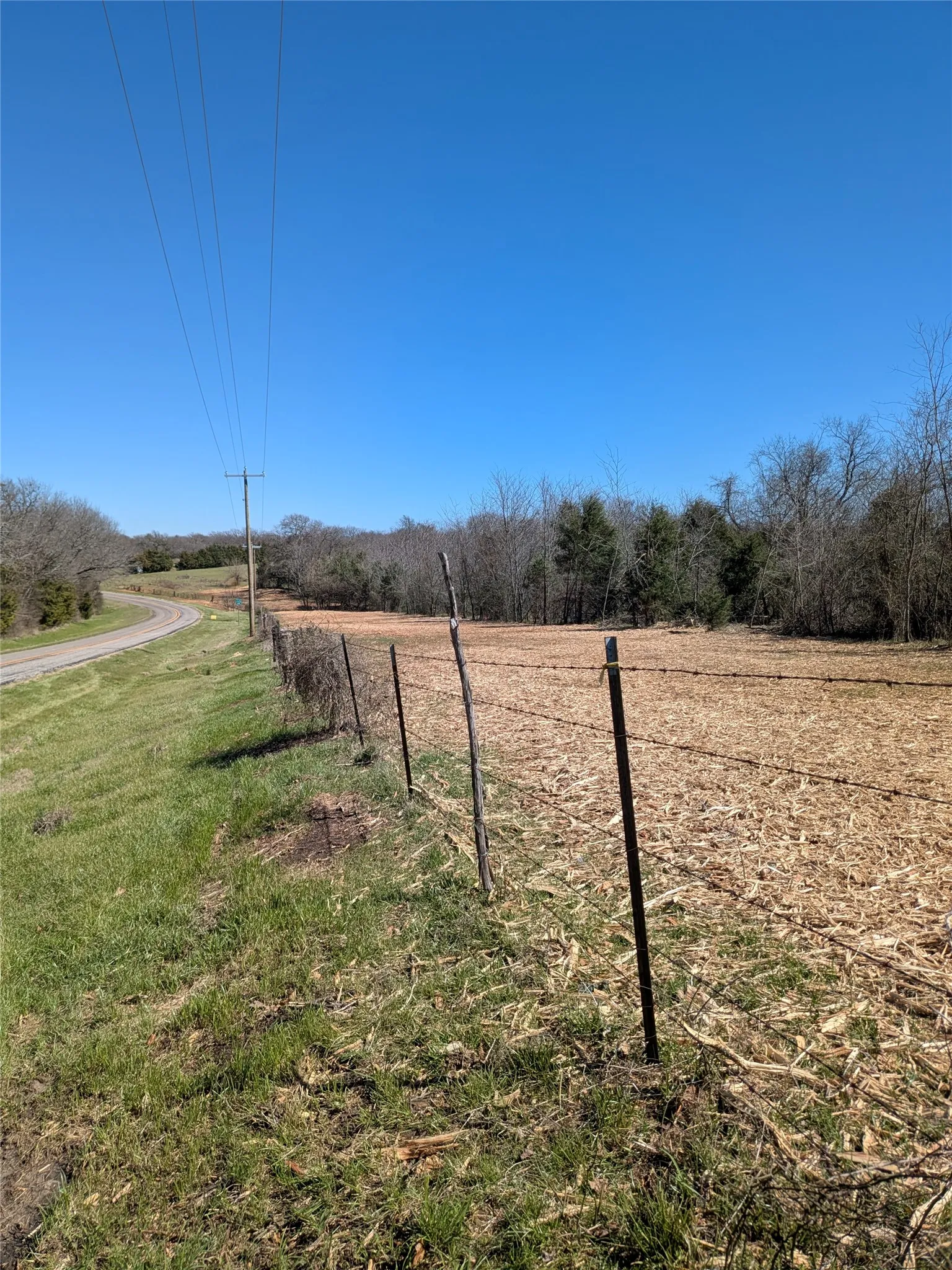 Expansive open field with partial fencing and surrounding natural tree line