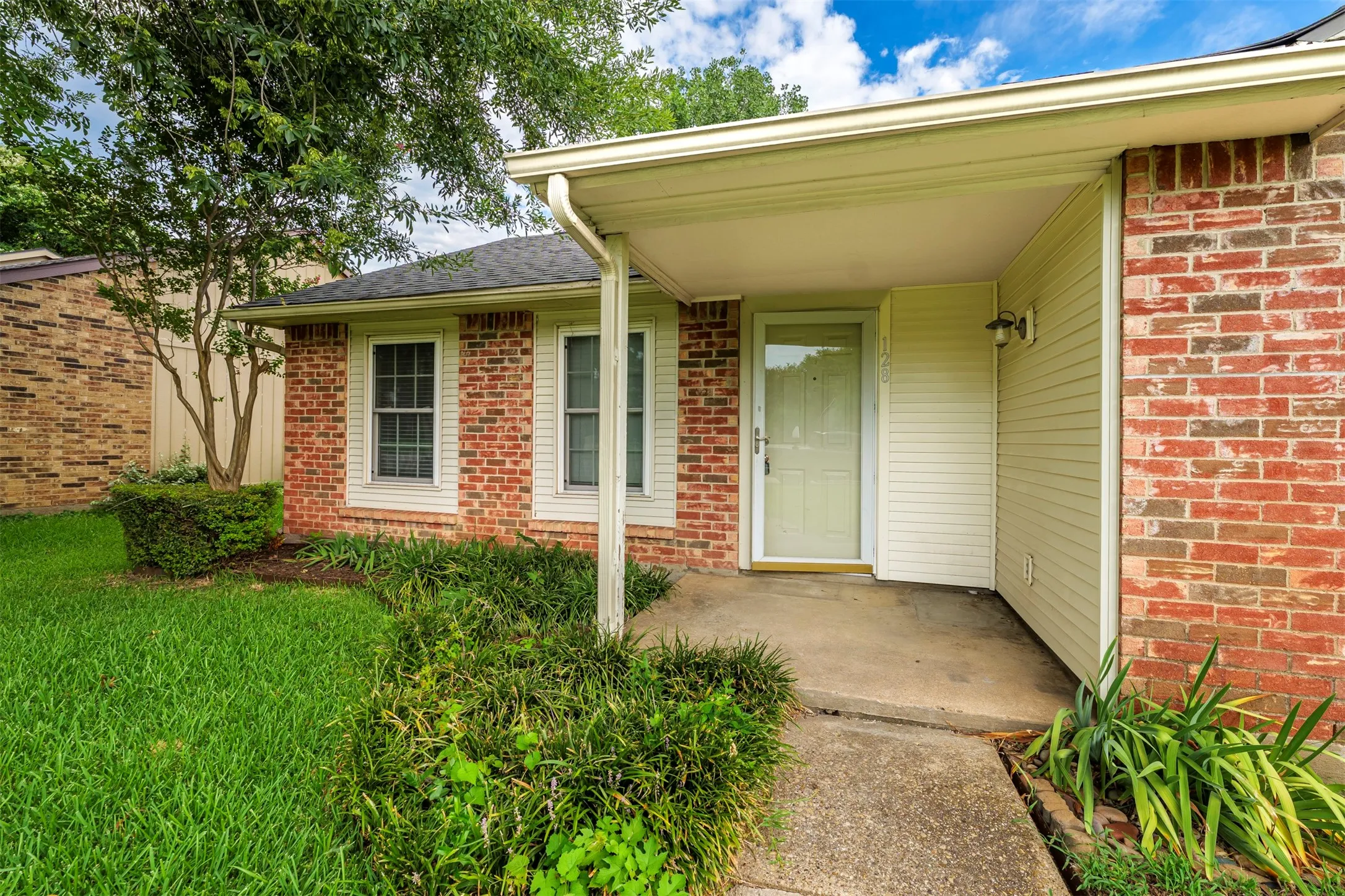 Brick and siding exterior featuring a covered entry, established landscaping, a concrete walkway, and a prominent front door