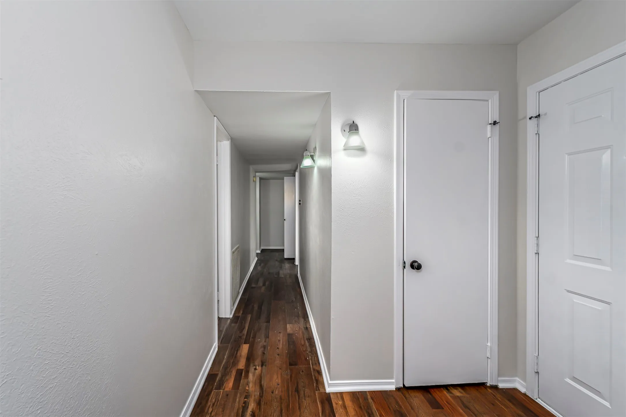 Hallway featuring wood-finish flooring, light grey walls, white trim, and wall-mounted sconces