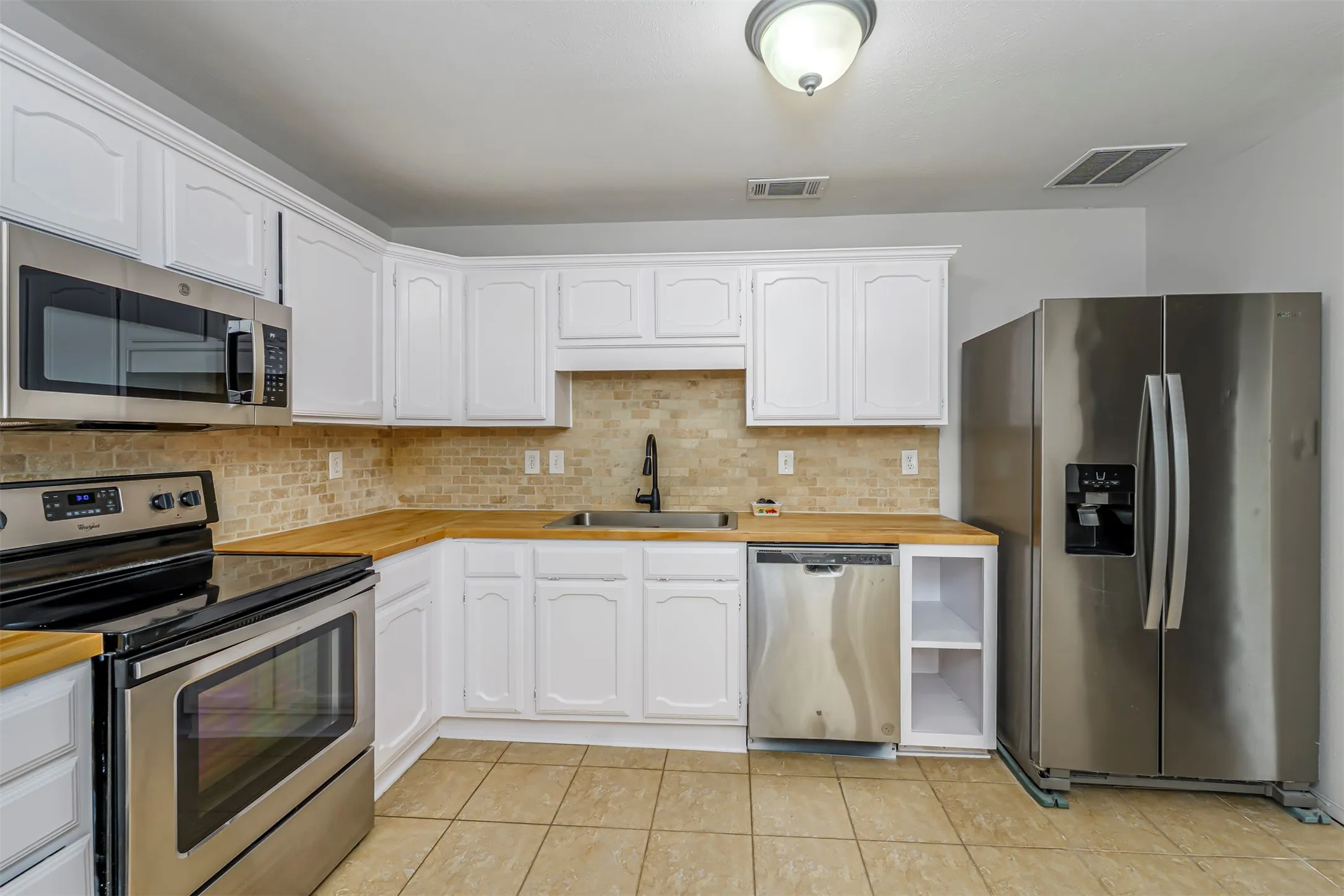 Updated kitchen featuring white cabinetry, wood-finish countertops, stainless steel appliances, a tiled backsplash, and tile flooring
