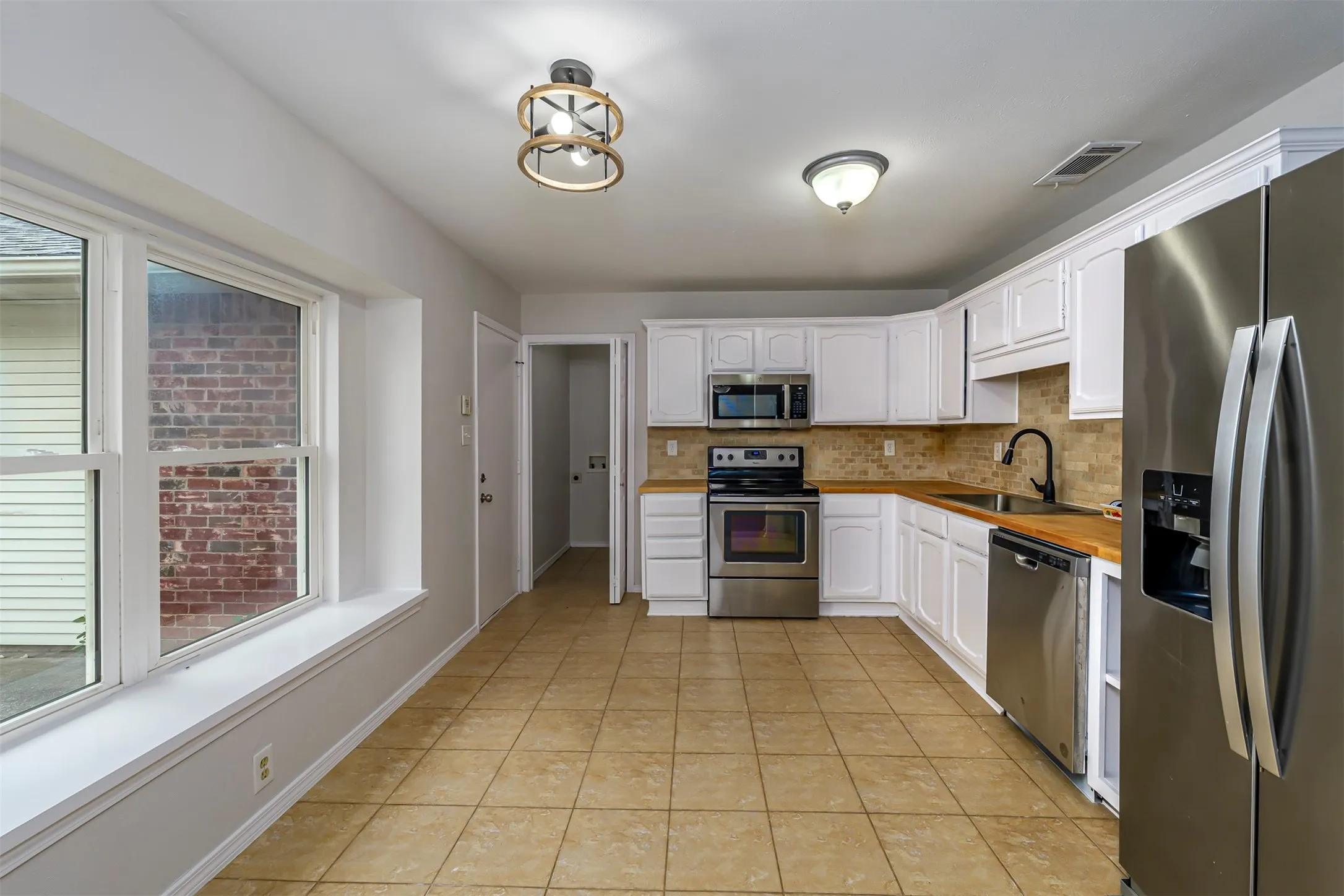 Kitchen featuring stainless steel appliances, wood-finish countertops, white cabinetry, and a neutral tile backsplash