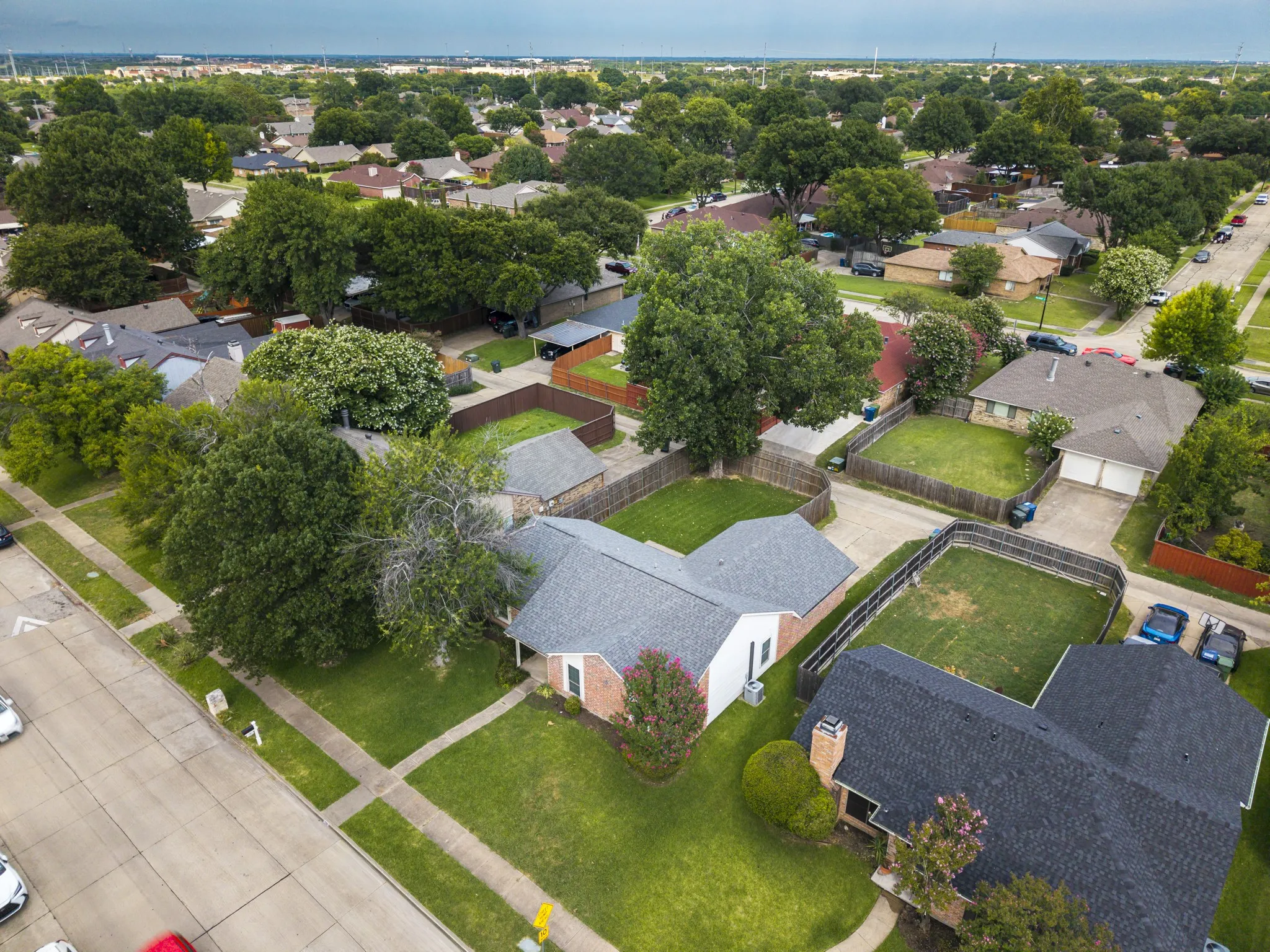 Single-story brick exterior featuring a gray shingle roof, mature front yard trees, and an established sidewalk