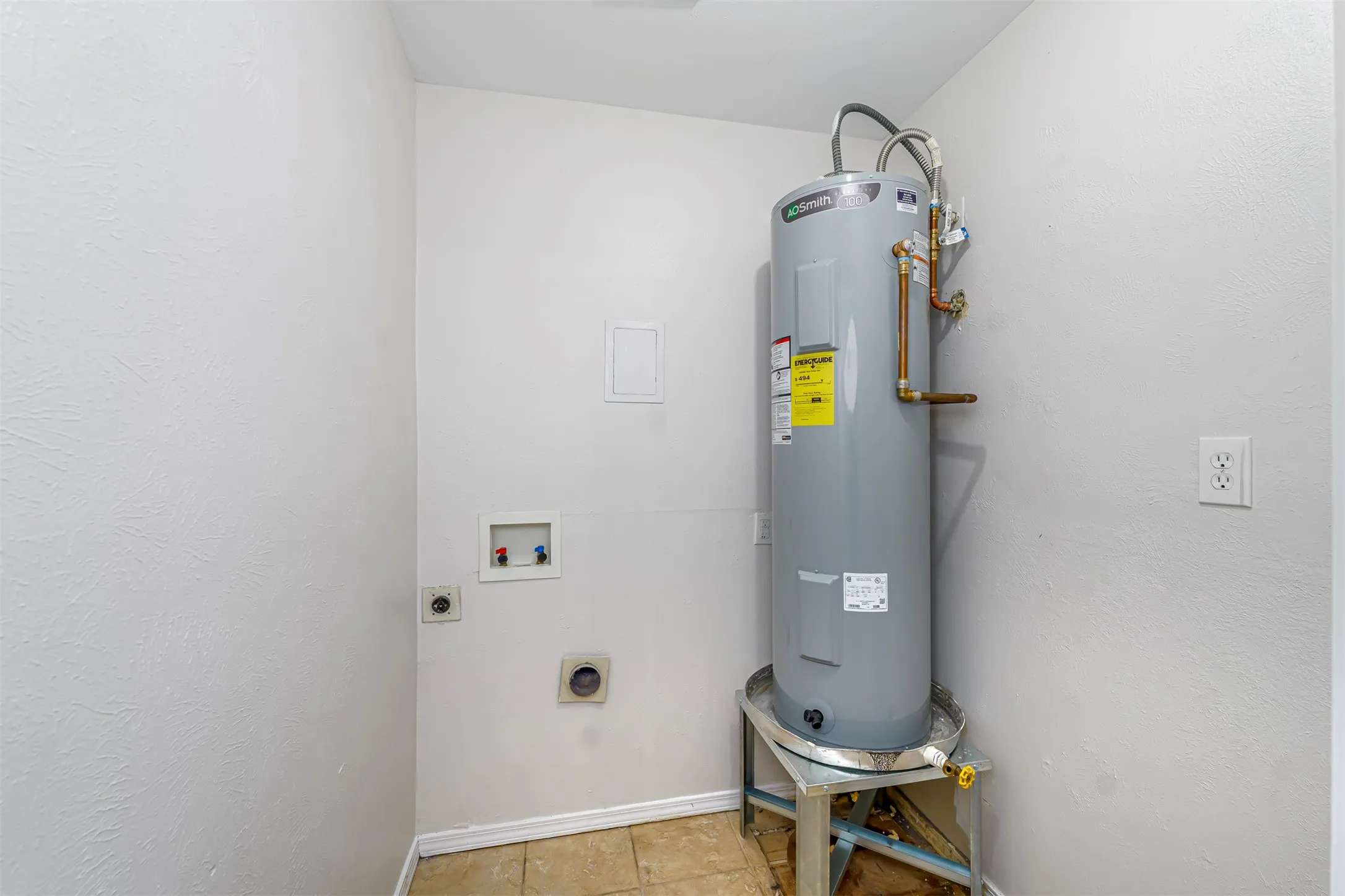 Dedicated utility space featuring a water heater, washer hookups, dryer vent, electrical outlet, and tile flooring