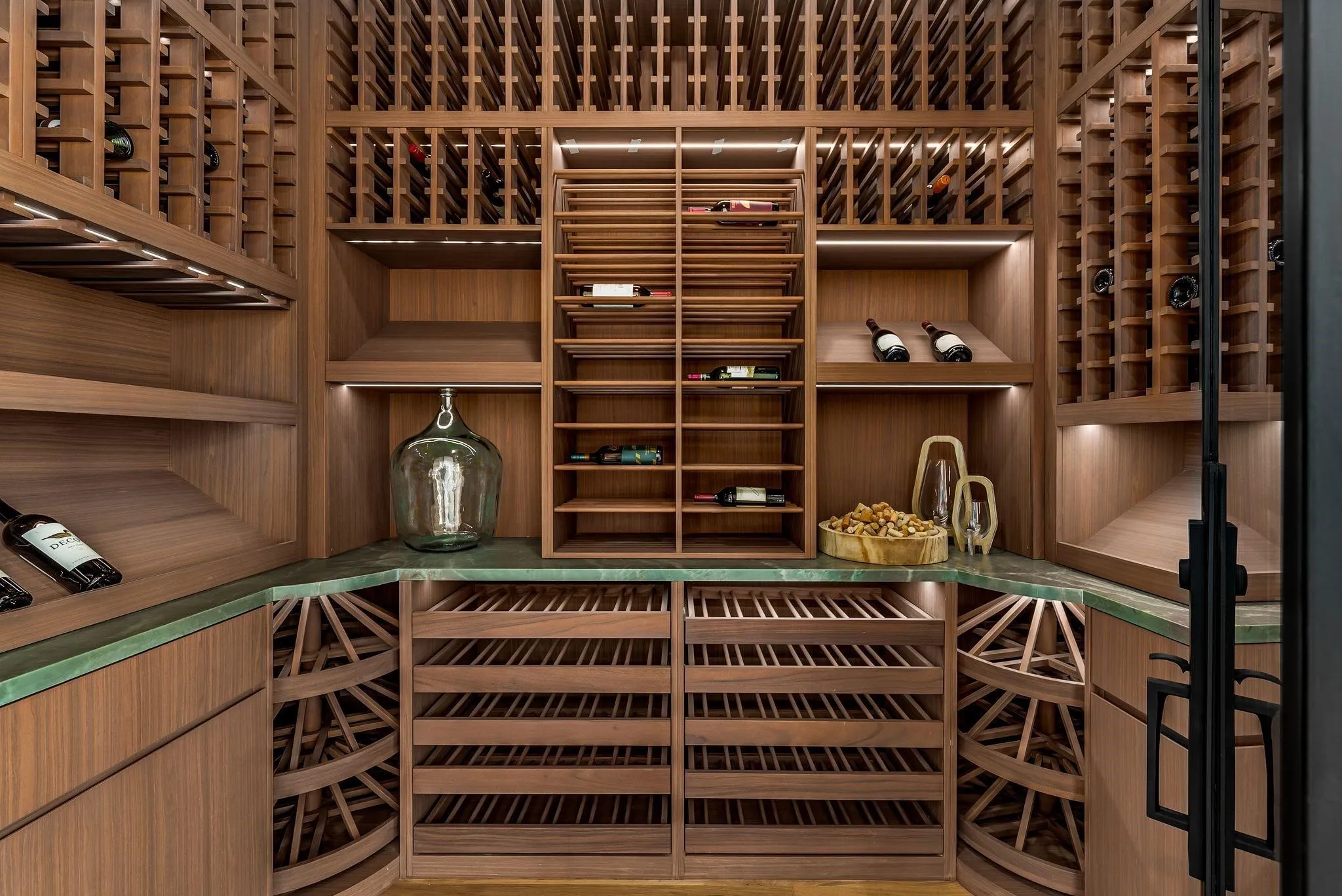 Custom wine cellar featuring extensive wooden racking, integrated shelving, and a green stone countertop