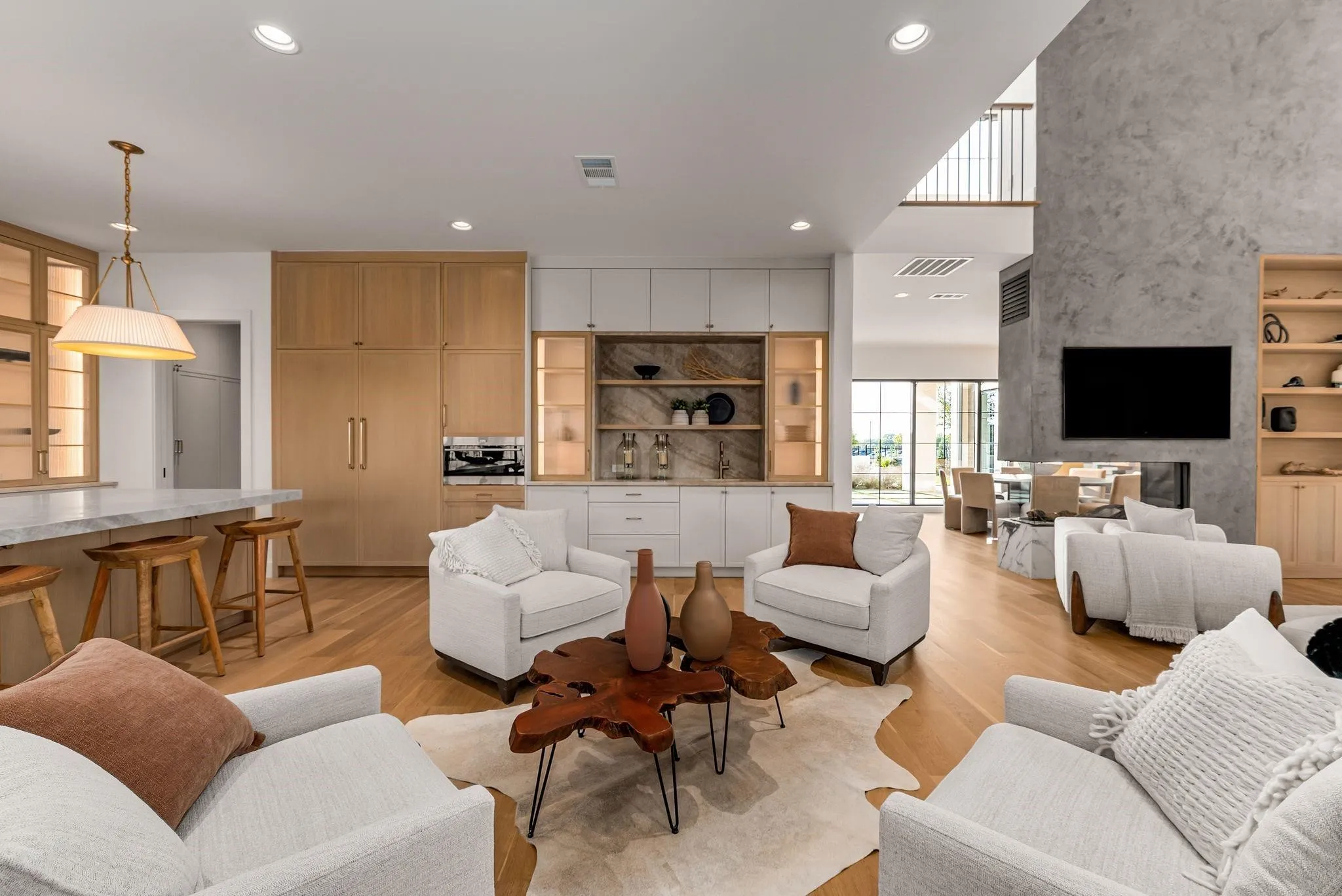 Spacious living area featuring light wood-finish flooring, a contemporary fireplace with a large textured surround, and a dry bar with integrated shelving