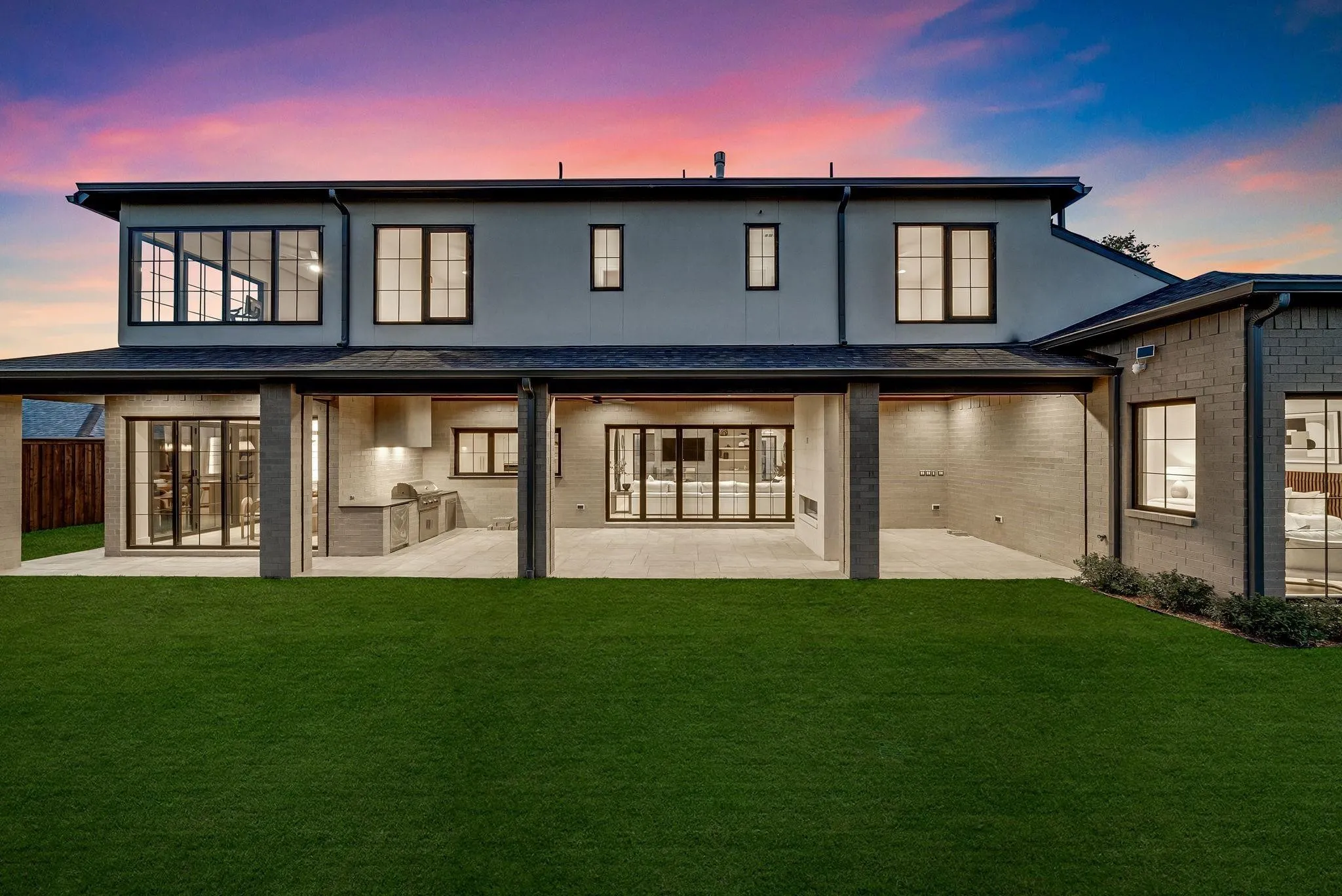 Rear exterior featuring a covered patio with an outdoor kitchen, bi-fold glass doors, a modern fireplace, and large format windows