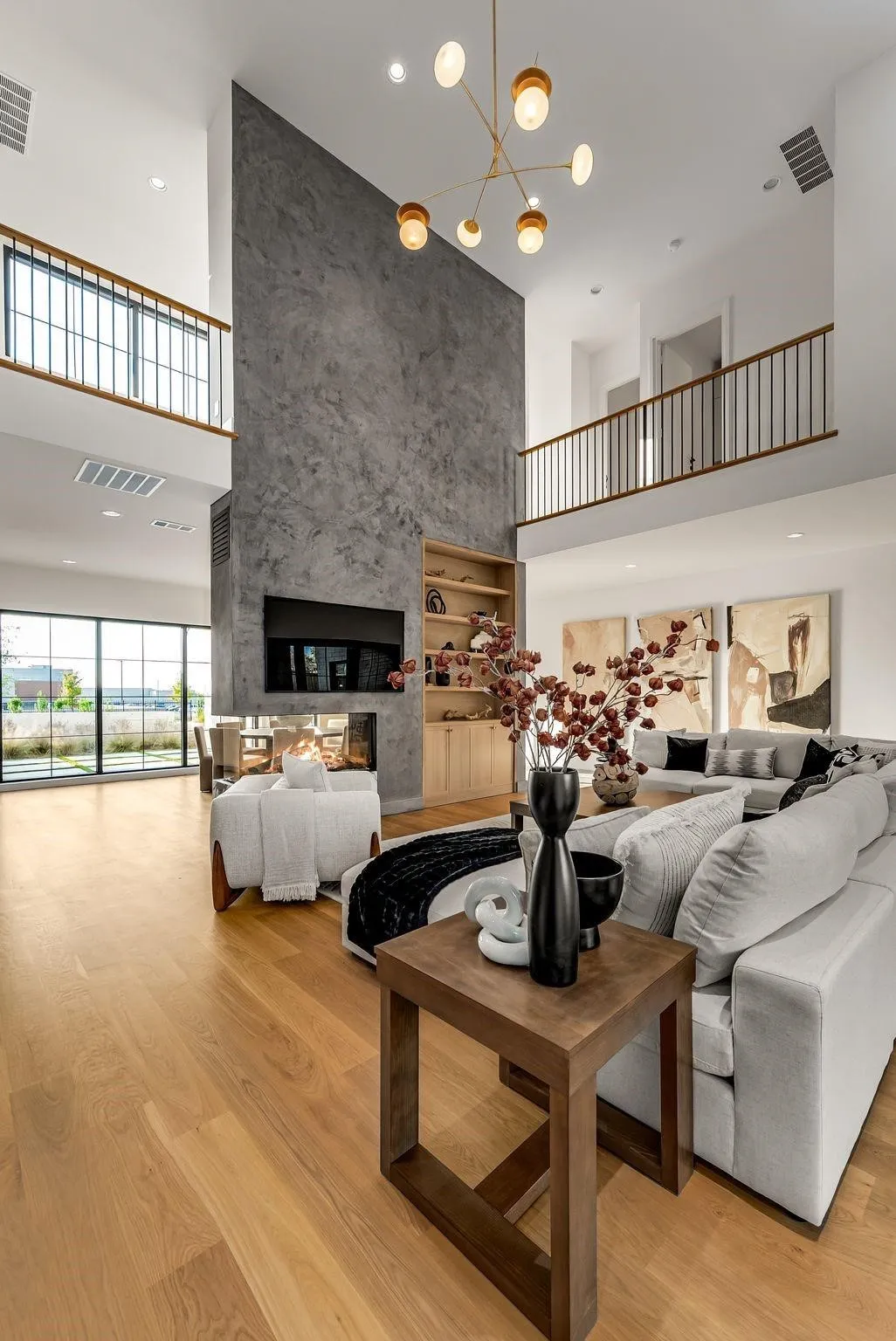 Two-story living area featuring a floor-to-ceiling textured fireplace, a built-in media center with shelving, wood-finish flooring, and a modern chandelier