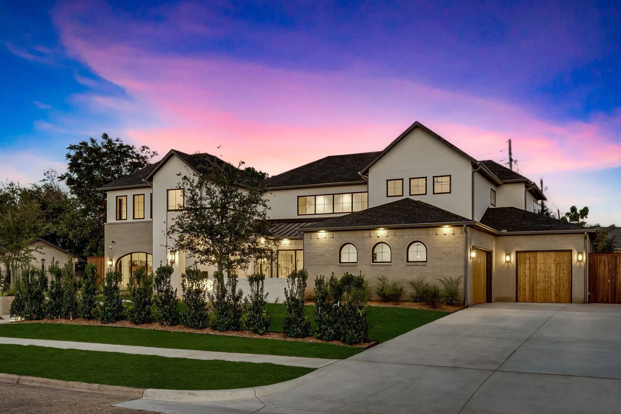 Contemporary residence featuring a two-car garage with wood-paneled doors, a curved concrete driveway, and established front landscaping