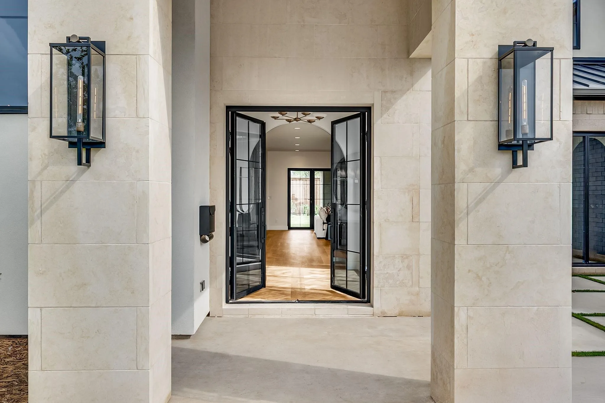 Grand entryway featuring a stone facade, double iron and glass doors, contemporary wall sconces, and a concrete patio
