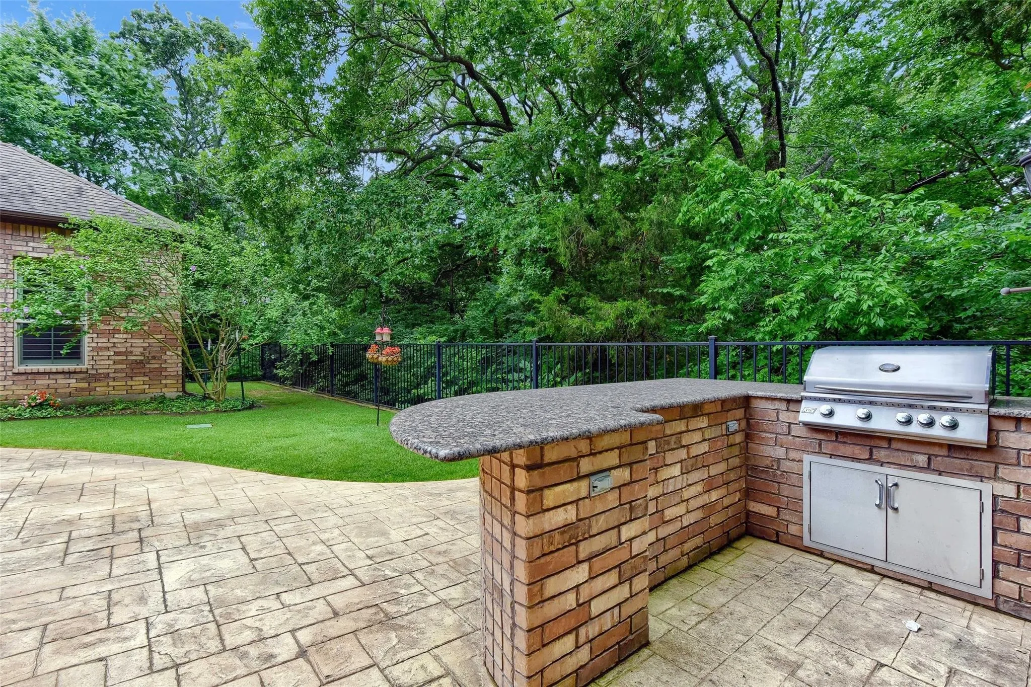 Expansive outdoor living area featuring a built-in brick grilling station with a stainless steel grill and storage, a stone-finish countertop, and a stamped concrete patio