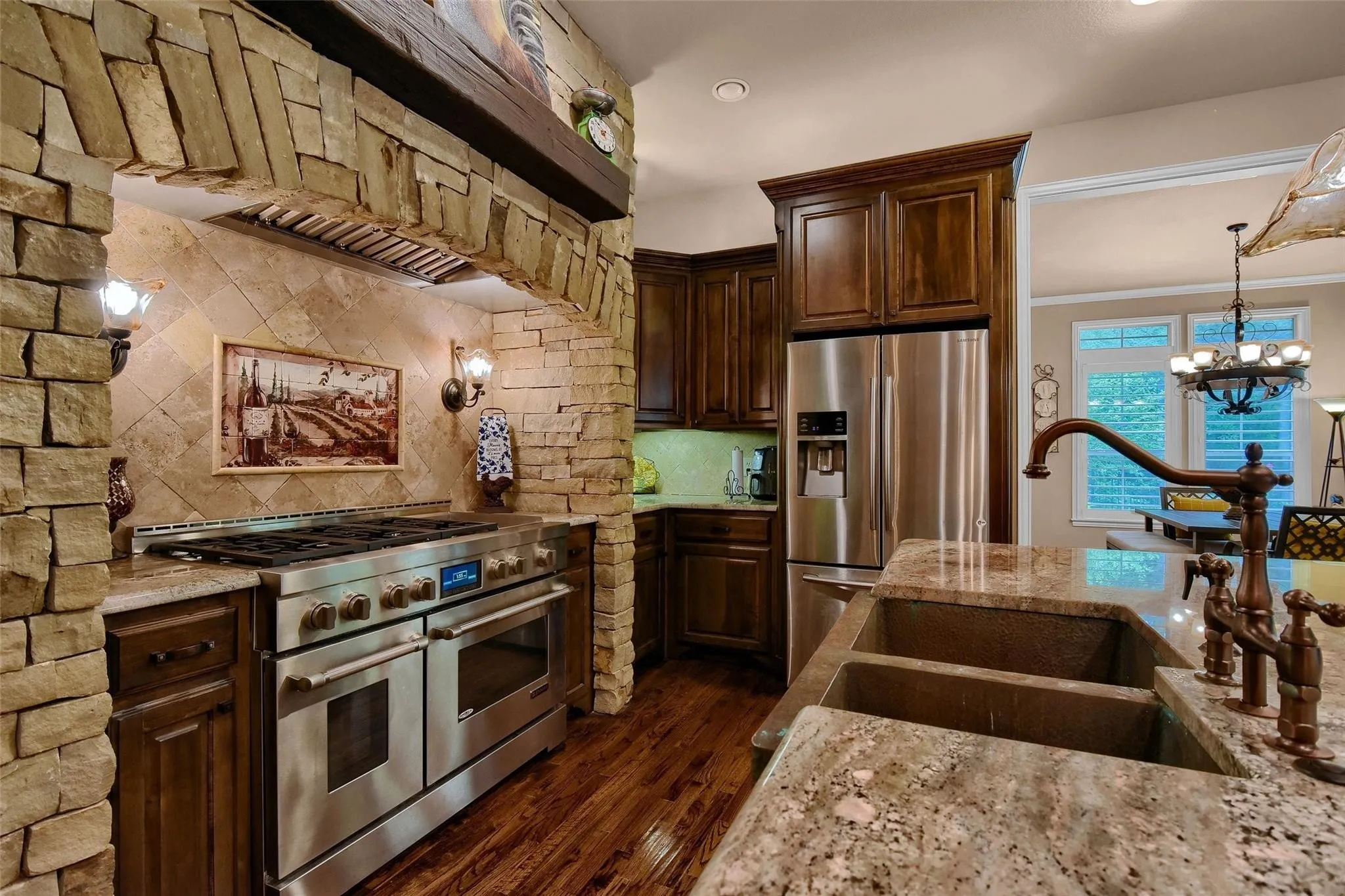 Gourmet kitchen featuring a stone archway with integrated lighting, a professional-grade stainless steel range, rich wood cabinetry, granite countertops, and wood-finish flooring