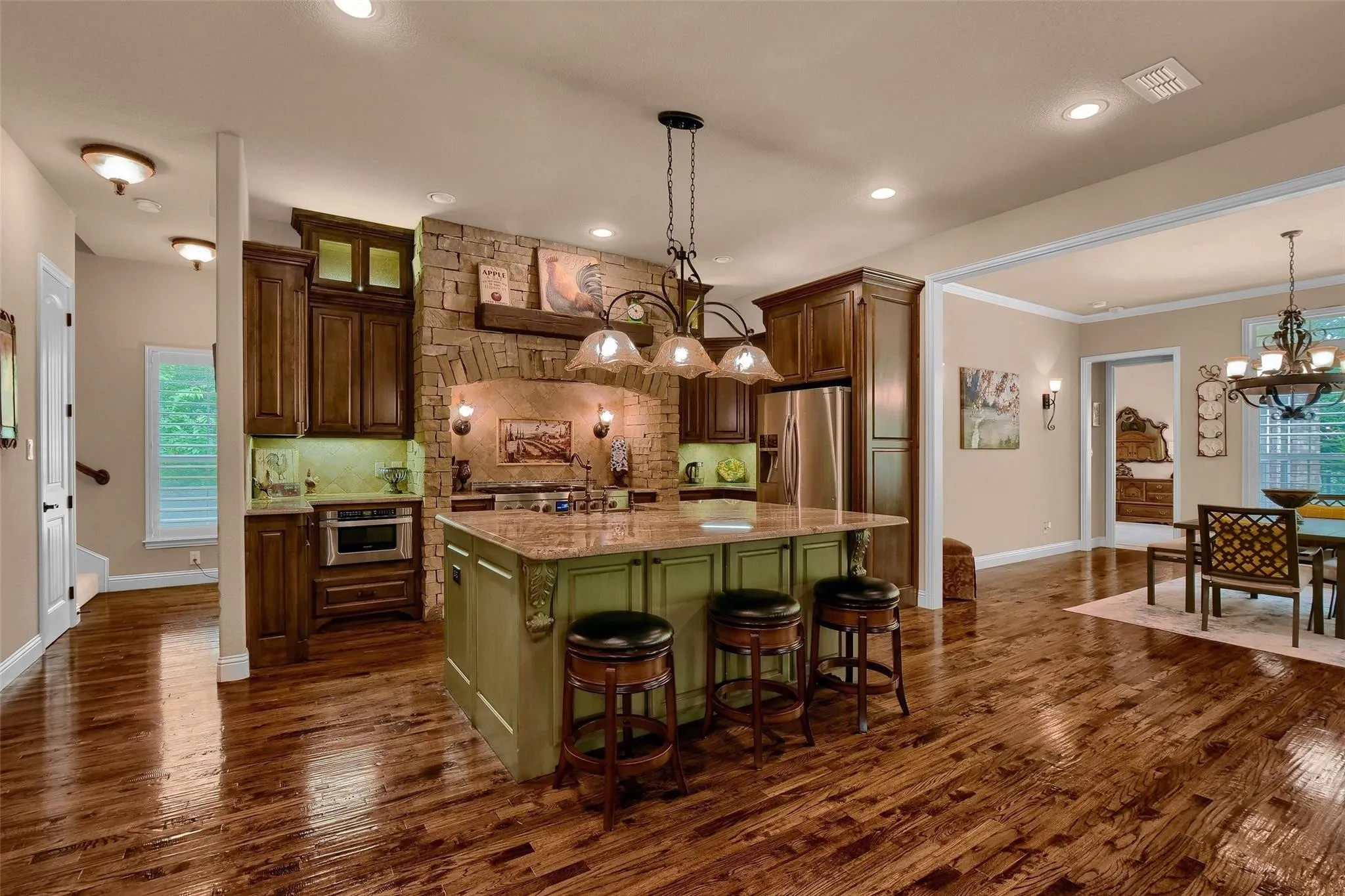 Gourmet kitchen featuring a stone archway, wood-finish flooring, custom cabinetry, a central island with countertop seating, and built-in stainless steel appliances