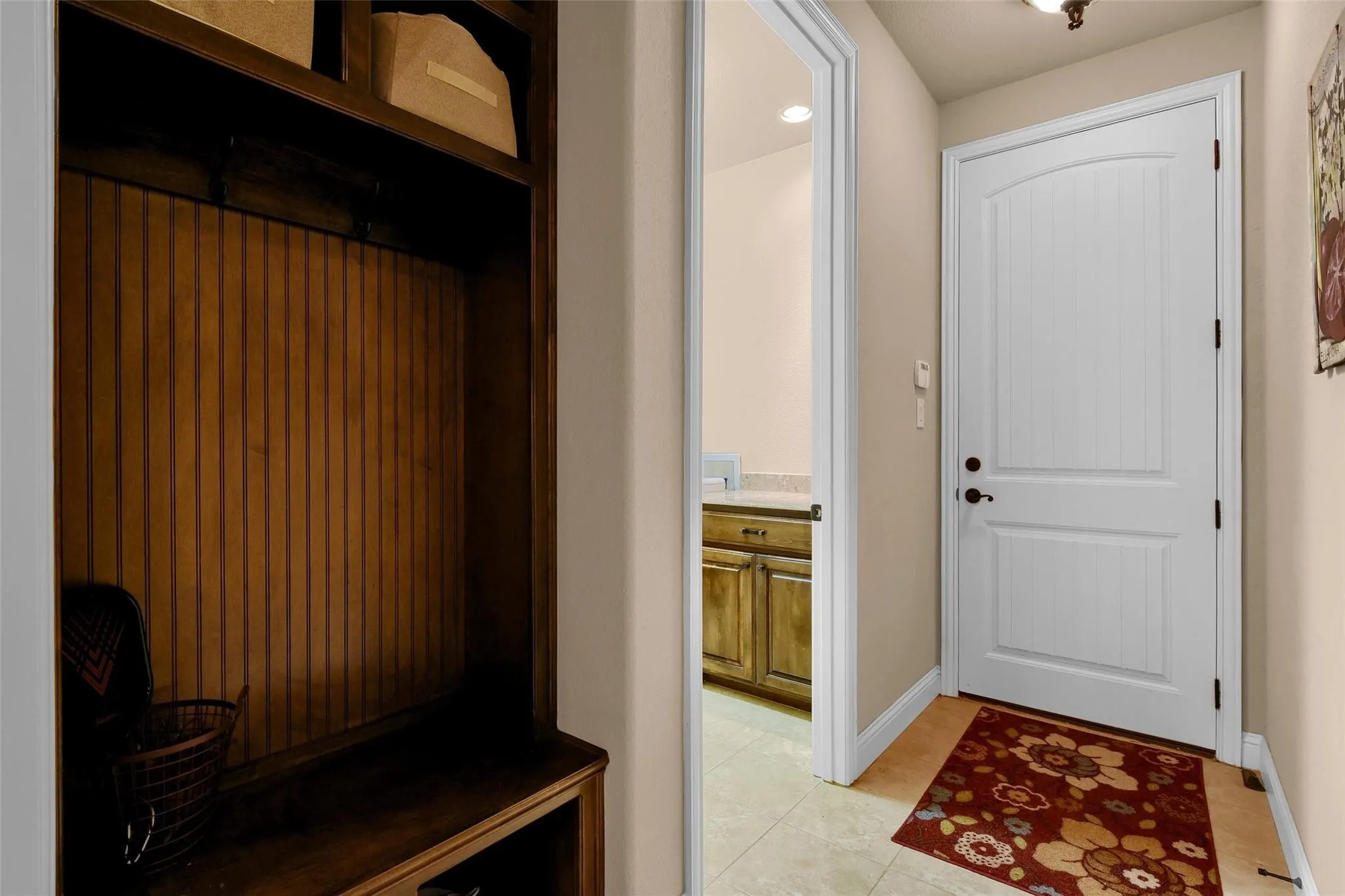 Mudroom area featuring a built-in wooden storage bench with beadboard backing, overhead shelving, and a durable tile flooring