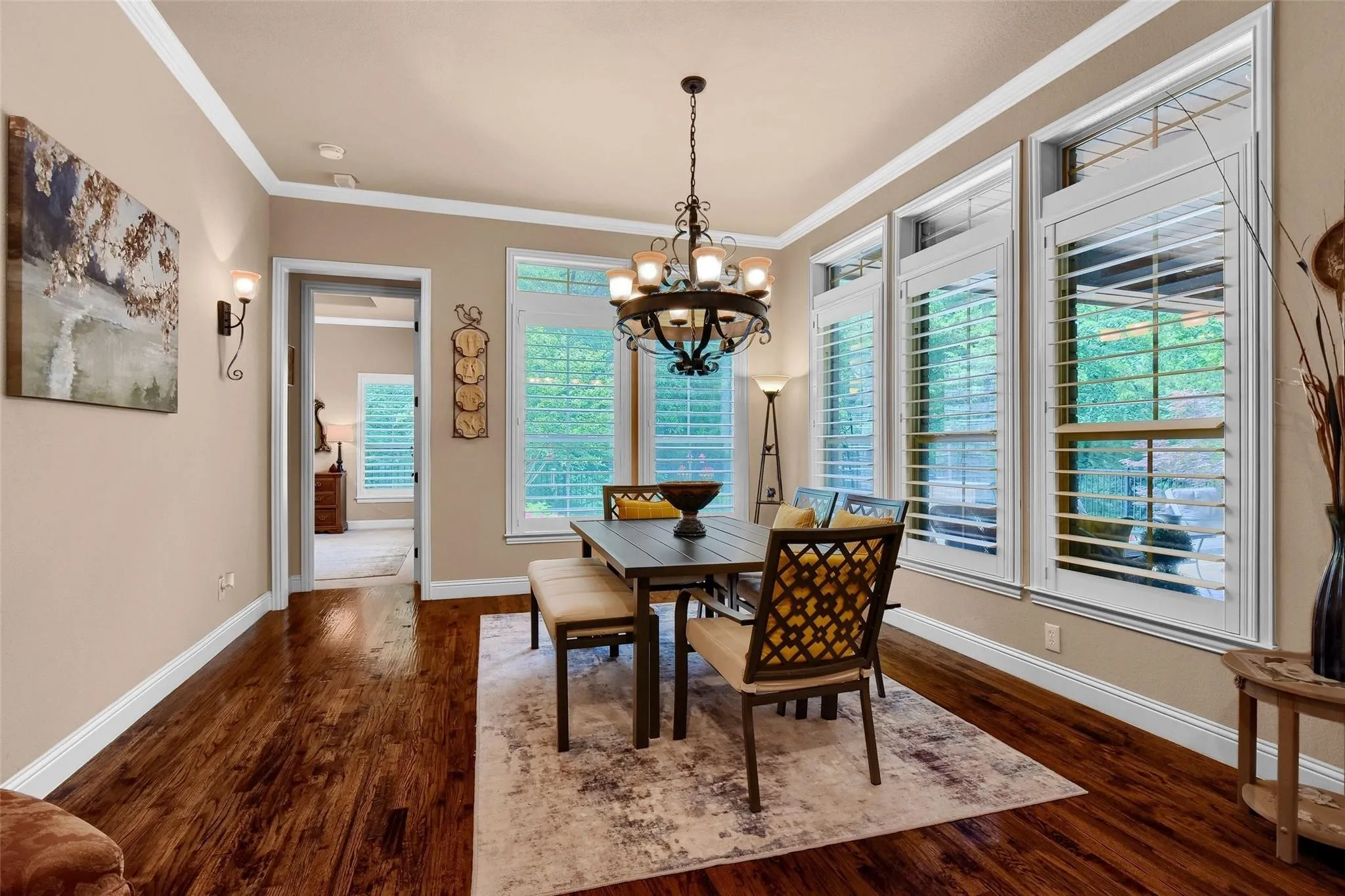 Dining area featuring rich wood-finish flooring, an ornate chandelier, and multiple windows with plantation shutters