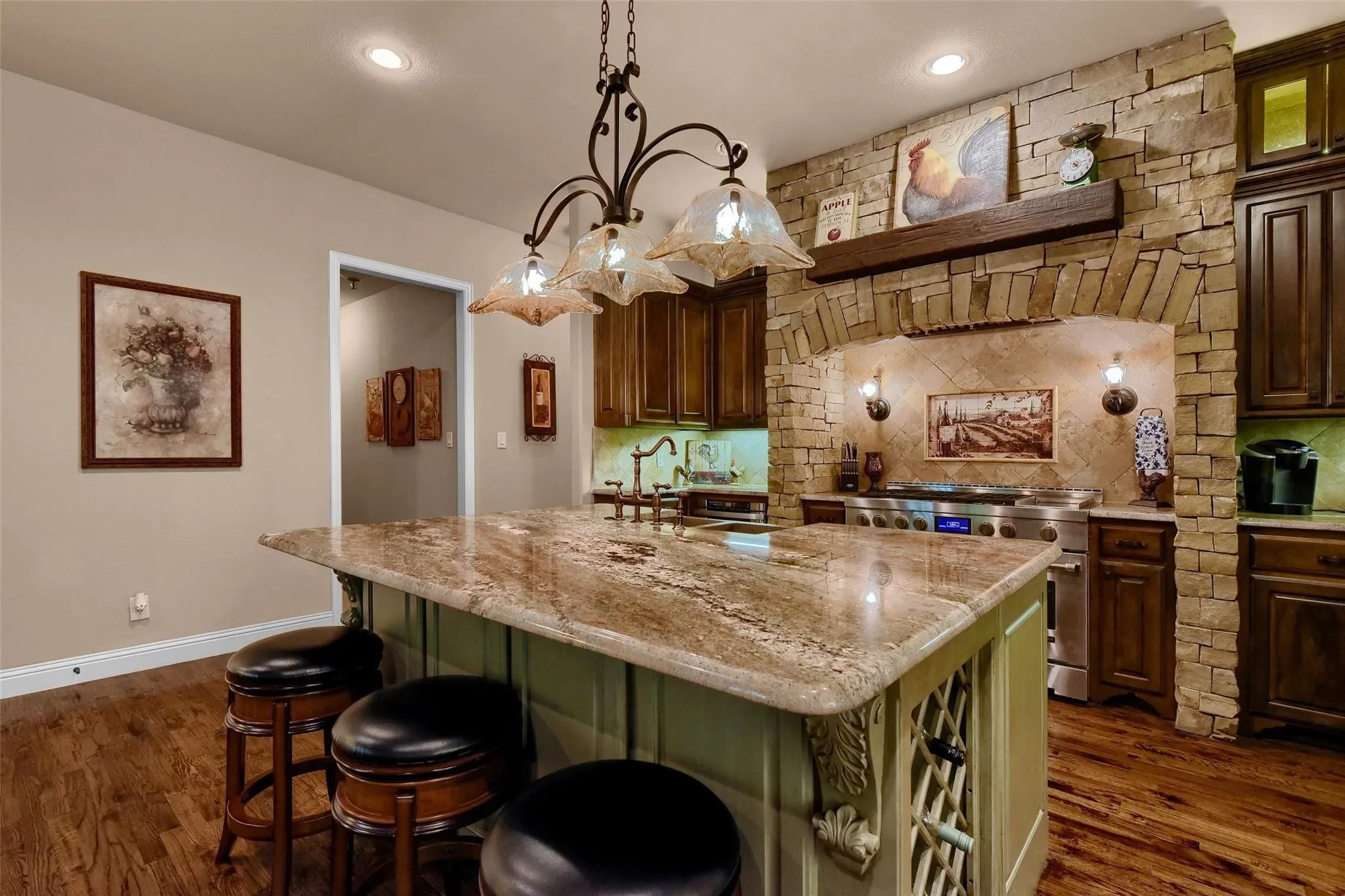 Gourmet kitchen featuring a large island with a stone countertop, custom cabinetry, hardwood flooring, and a stone-clad cooking alcove with an integrated range