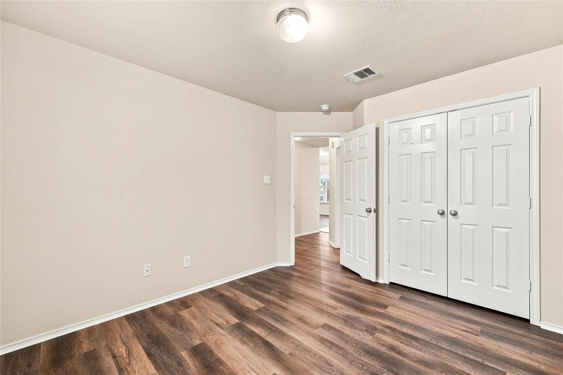 Room featuring wood-finish flooring, light-toned walls, white baseboards, and a ceiling-mounted light fixture