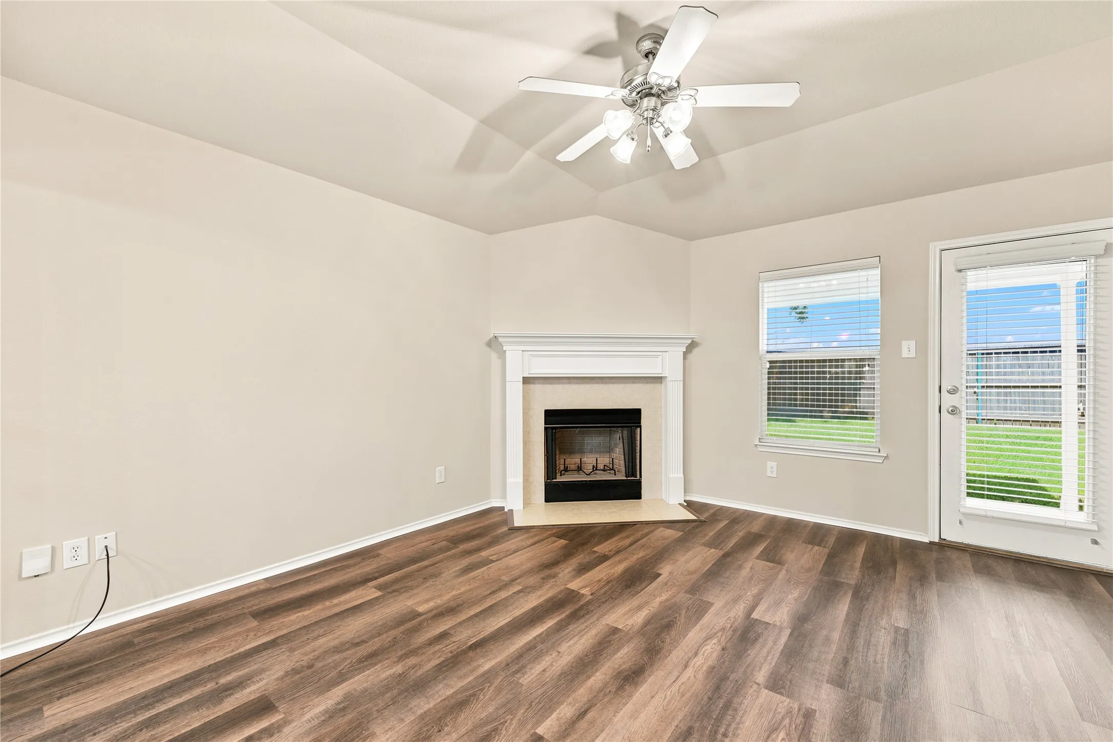 Living area featuring wood-finish flooring, a corner fireplace with a white mantel, and a ceiling fan