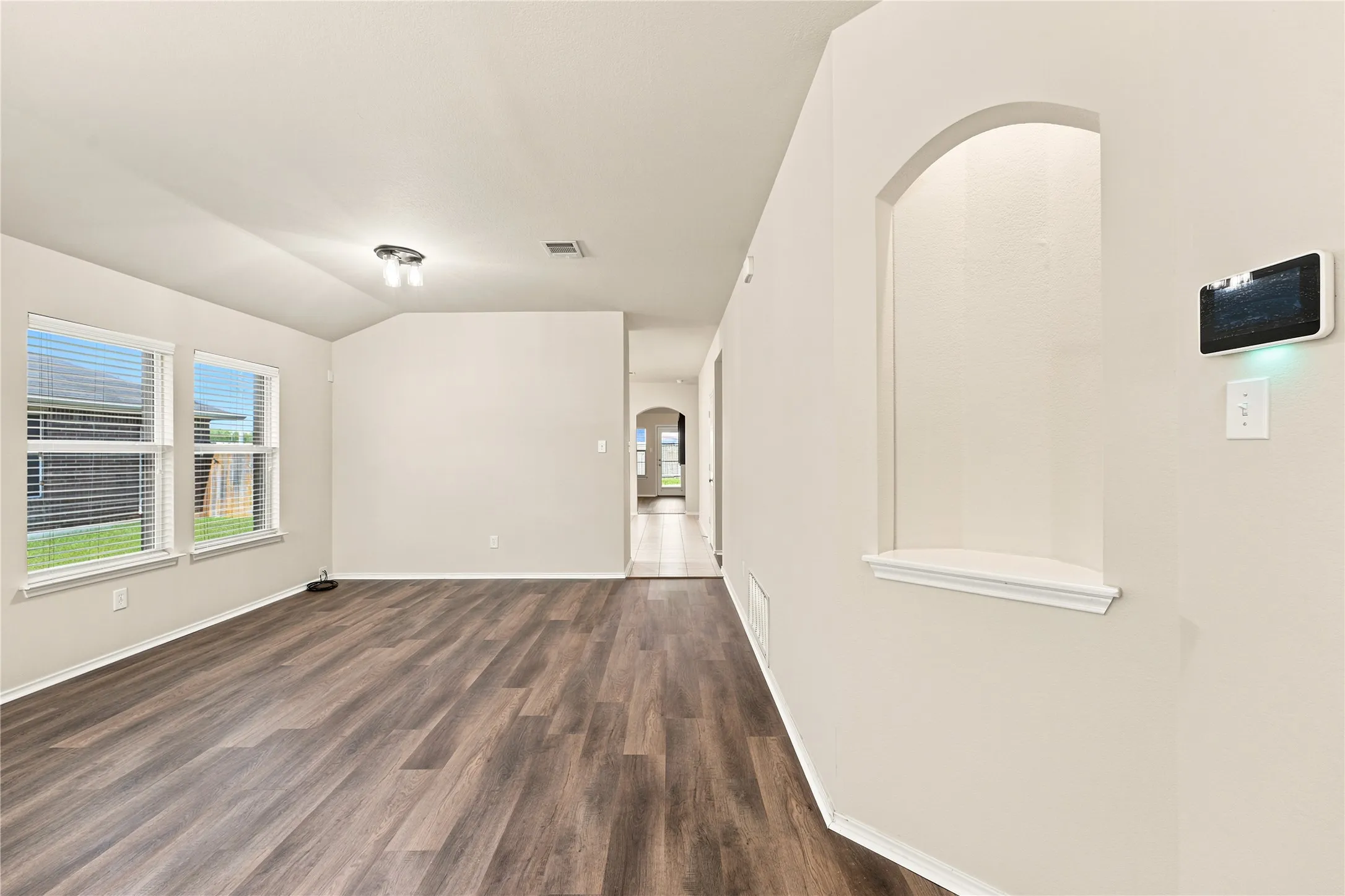 Spacious room featuring wood-finish flooring, light-colored walls, and multiple windows with blinds
