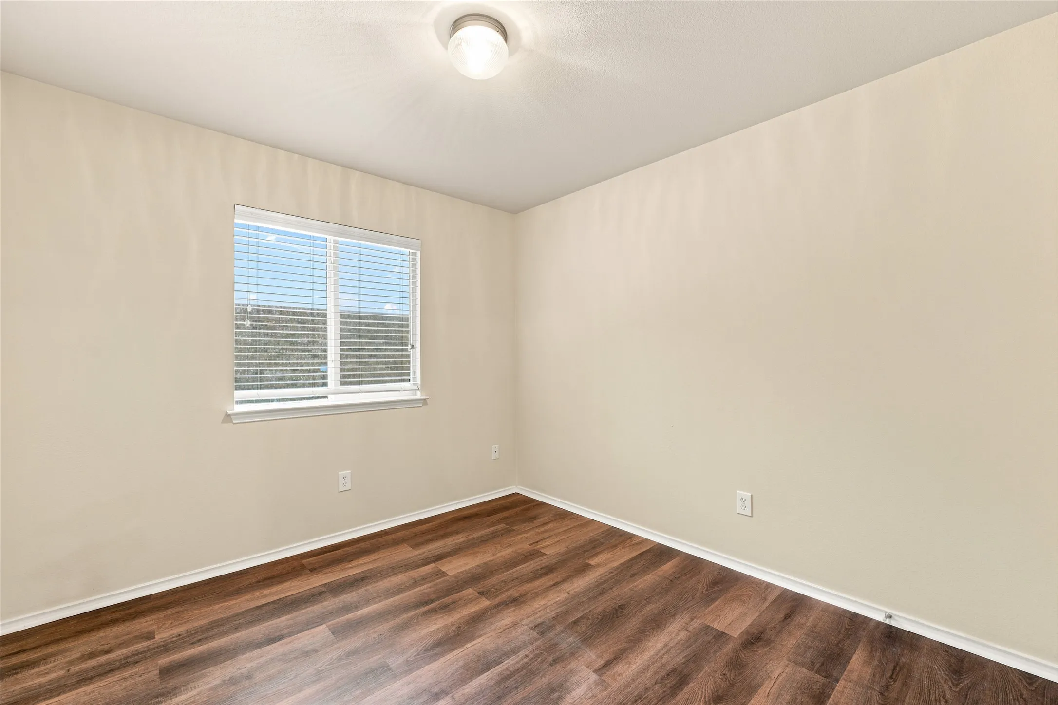 Room with wood-finish flooring, a double-hung window with blinds, and a flush mount ceiling light fixture