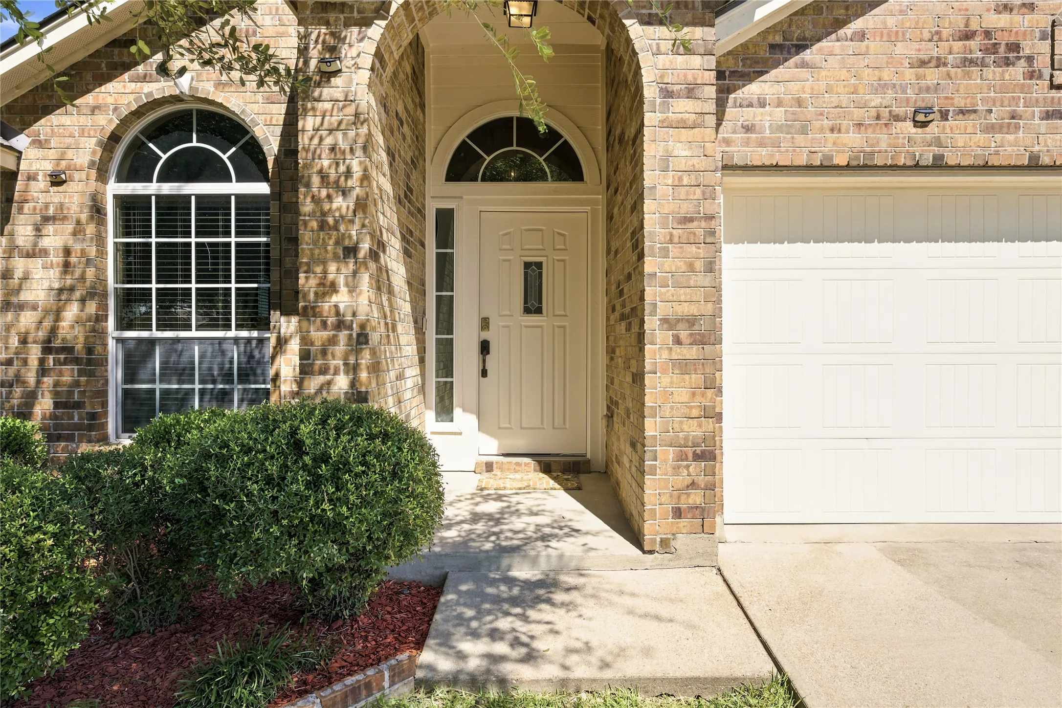 Brick exterior featuring an arched entryway with sidelights, a paneled front door, and an arched window with grilles