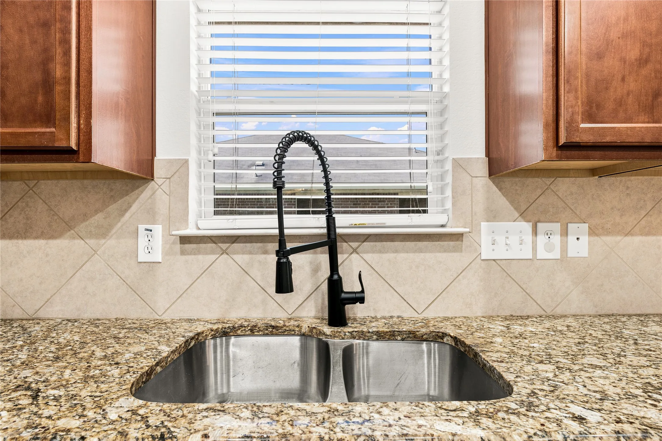 Double basin stainless steel sink with a matte black pull-down faucet, set into a granite countertop