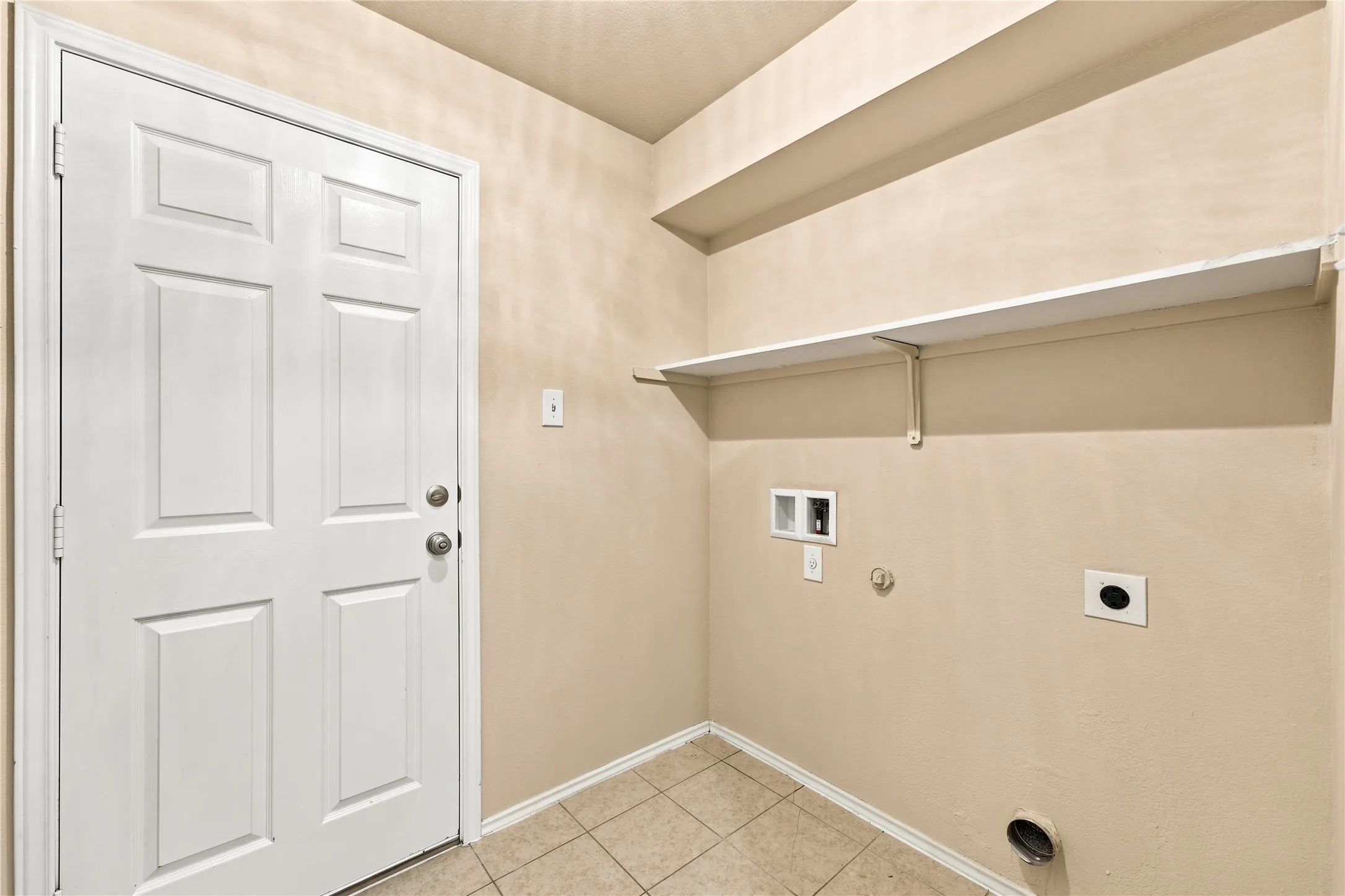 Dedicated laundry area featuring tile flooring, a white paneled door, and integrated shelving