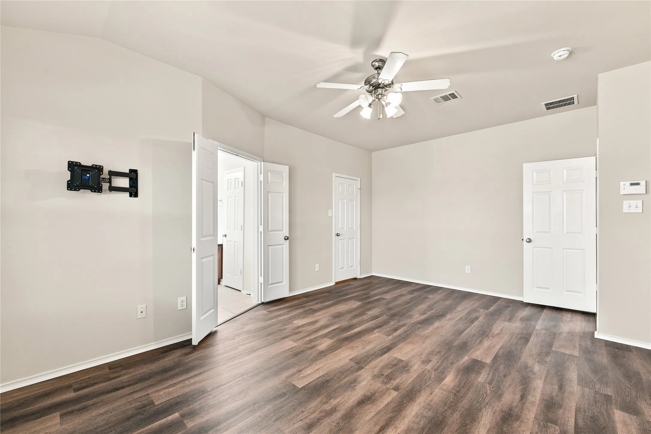 Spacious room featuring wood-finish flooring, light-toned walls, and a ceiling fan with integrated lighting