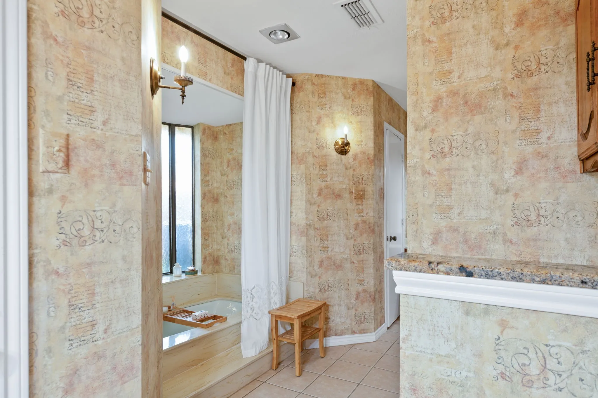 Bathroom featuring a built-in tub with step, decorative wall finishes, and a granite-topped half-wall