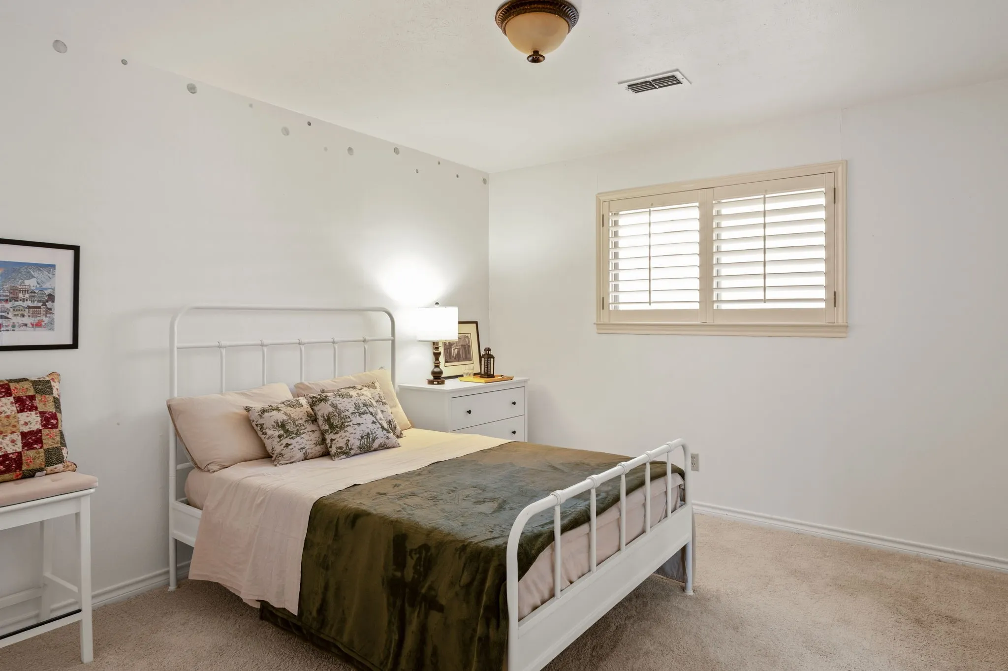 Carpeted room with a ceiling-mounted light fixture, white walls, and a window featuring light-colored plantation shutters