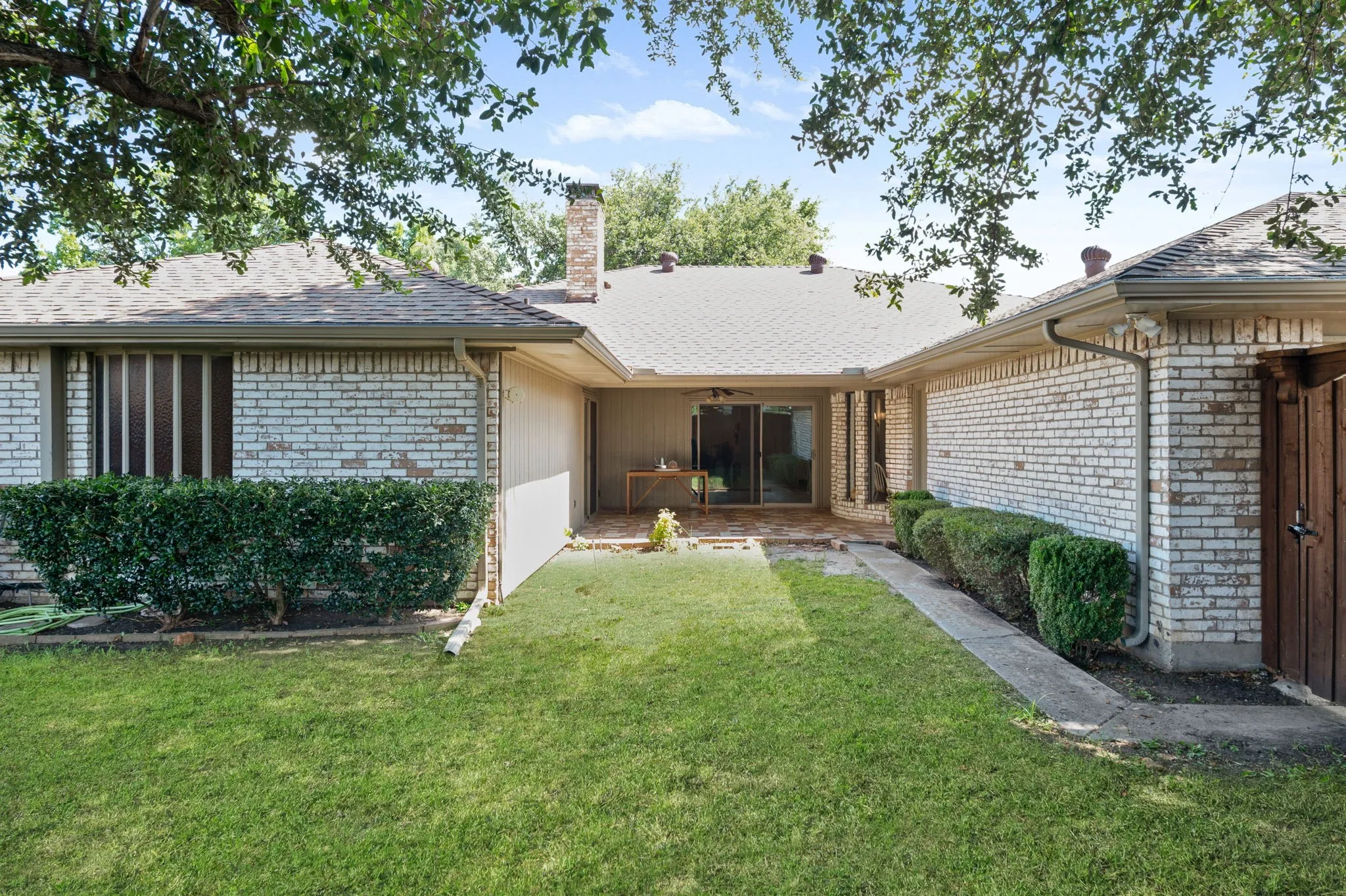 Expansive backyard featuring a concrete patio, sliding glass door access, light brick exterior, and mature landscaping
