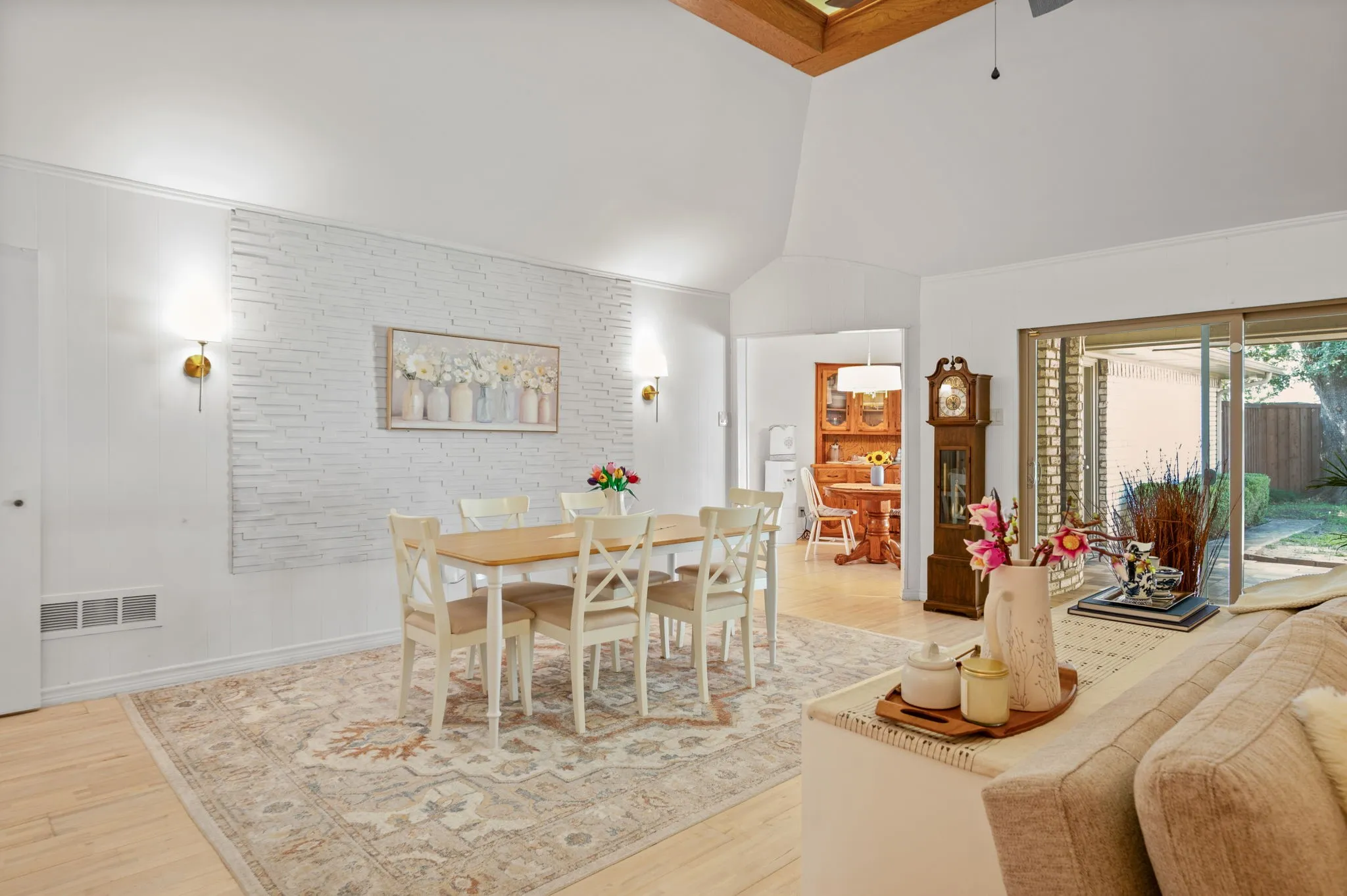Vaulted ceiling dining area featuring light wood-finish flooring, a white brick accent wall with wall sconces, and sliding glass door access to the exterior