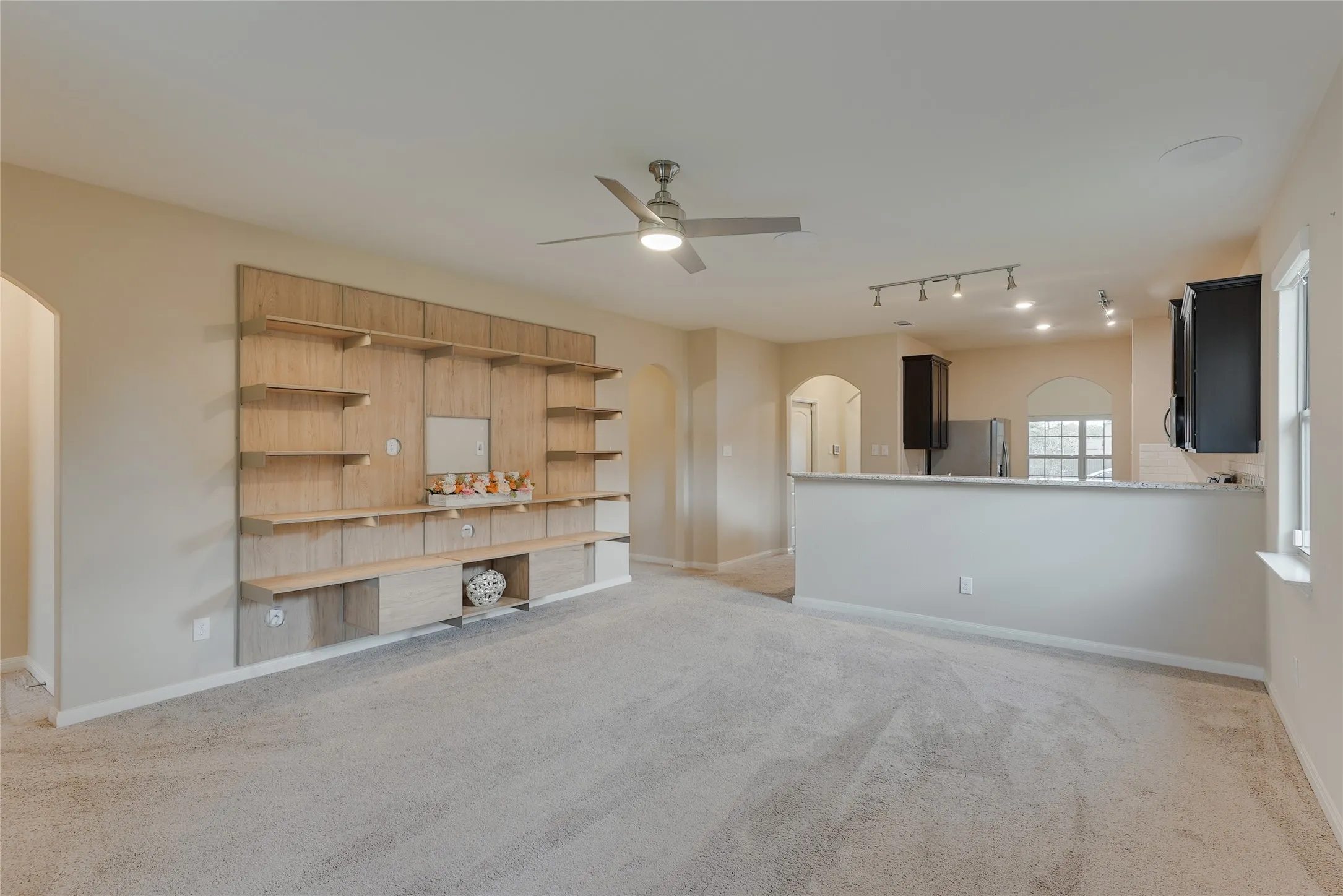 Spacious living area featuring a built-in wood-finish shelving unit, light gray carpeting, and a ceiling fan