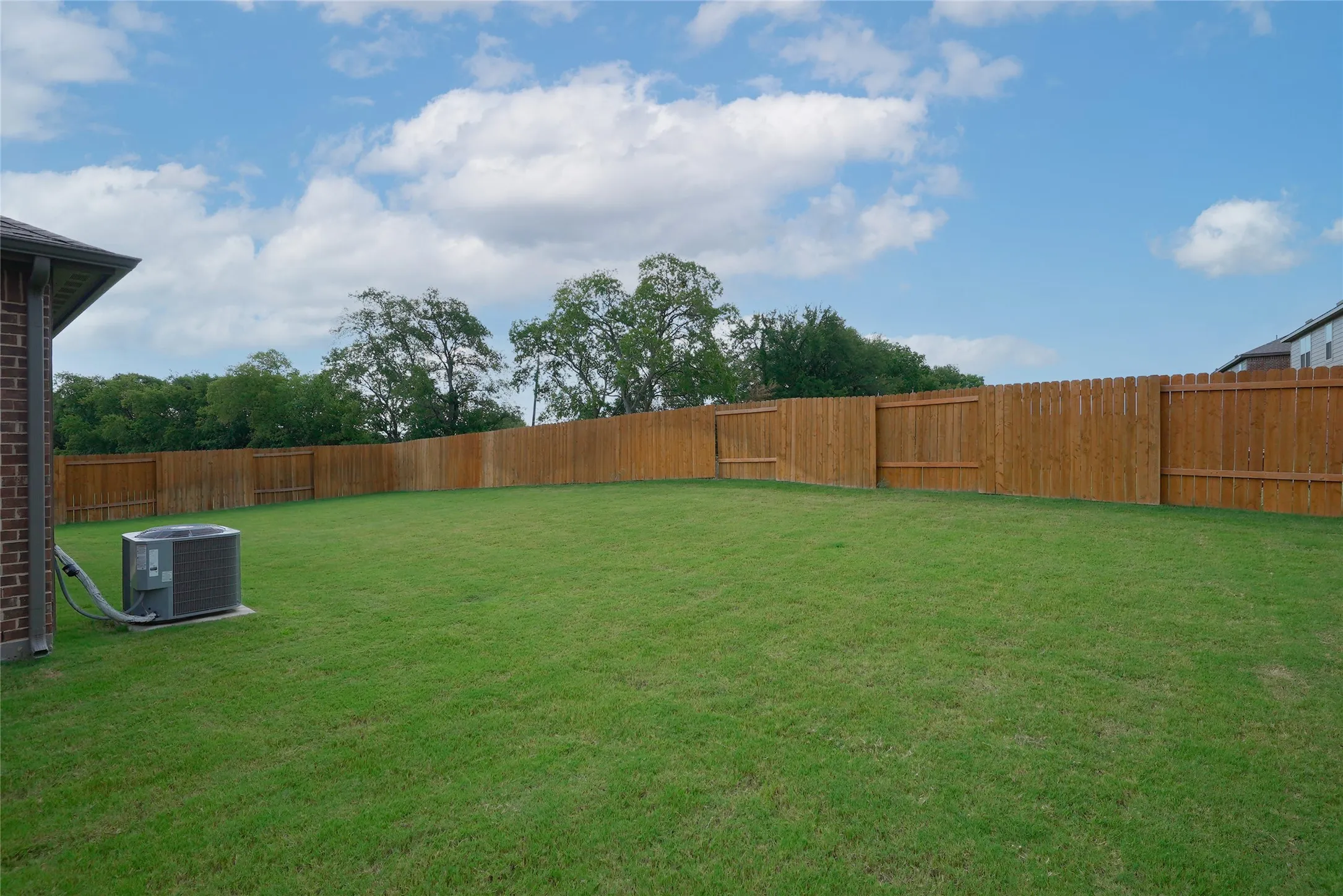 Spacious backyard featuring a substantial wooden privacy fence, manicured lawn, and mature perimeter trees