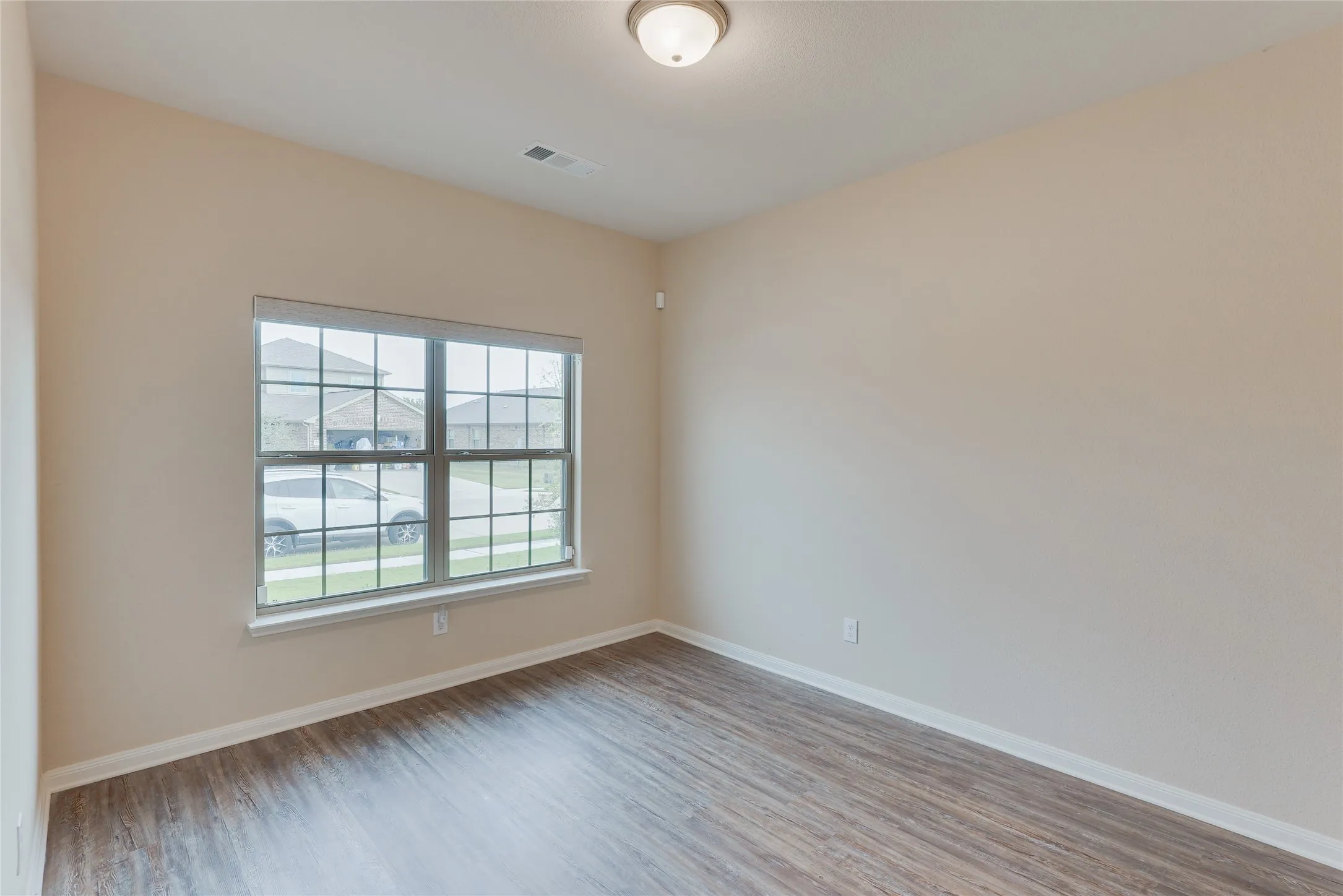 Room featuring wood-finish flooring, neutral wall tones, and a large window with blinds