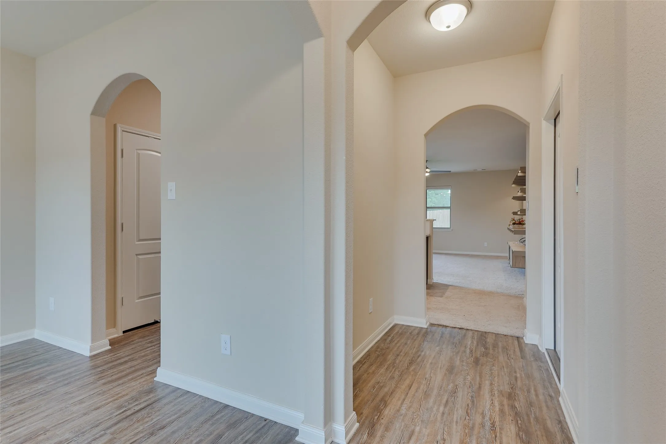 Arched doorways leading from a hallway with wood-finish flooring into a carpeted room