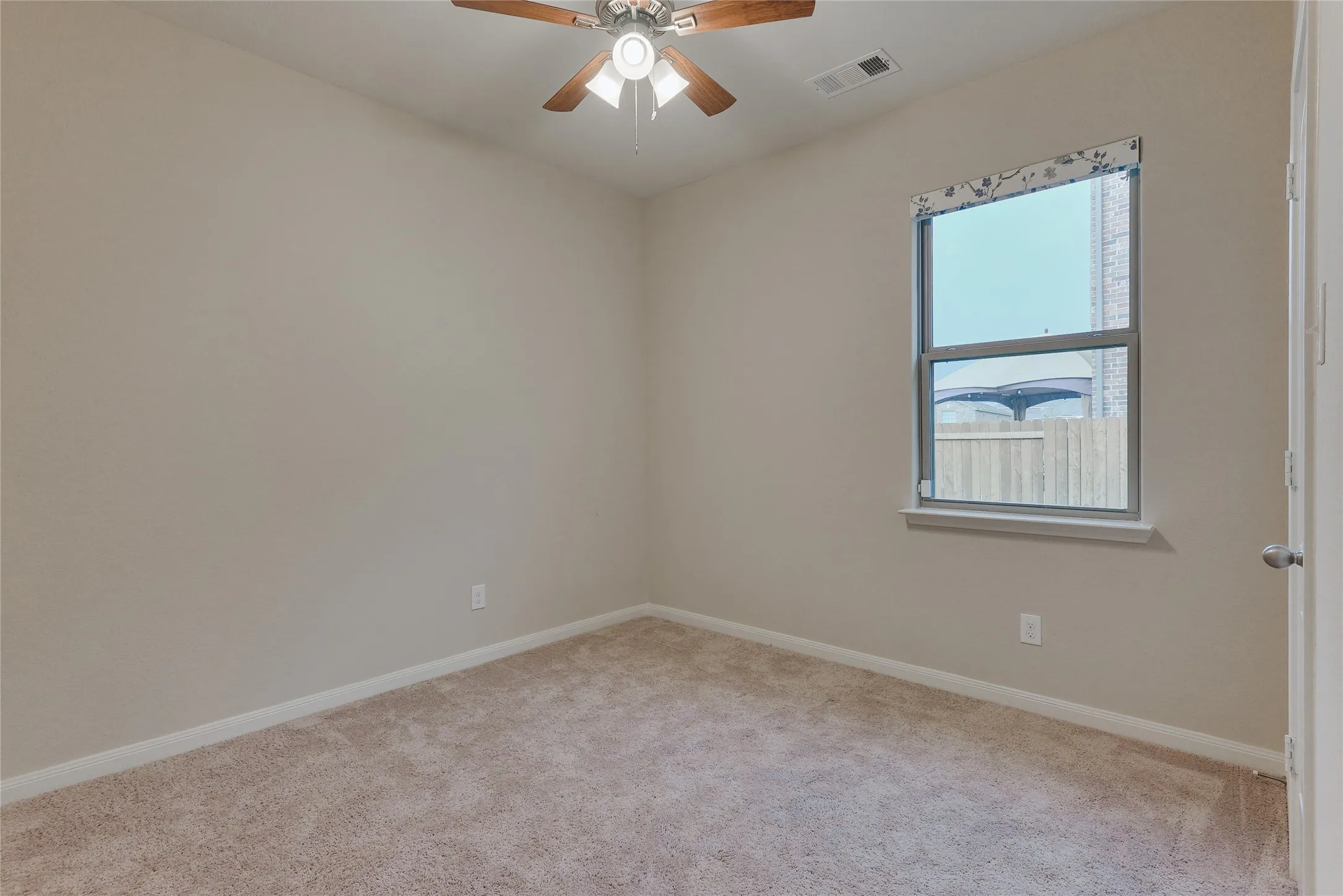 Room featuring neutral wall finishes, light-toned carpet, a ceiling fan with wood-finish blades, and a single window with a white sill