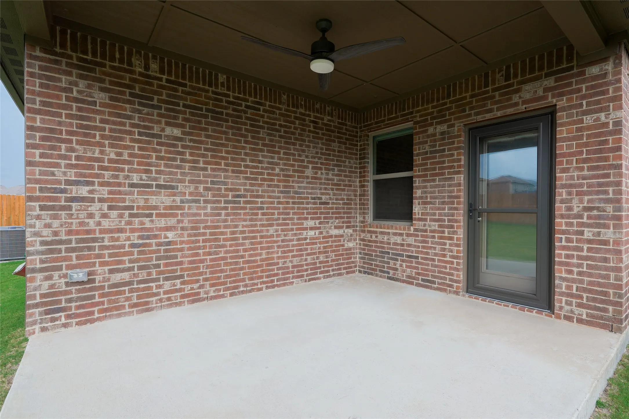 Covered concrete patio featuring a ceiling fan with integrated lighting, brick exterior, and a glass-paneled door