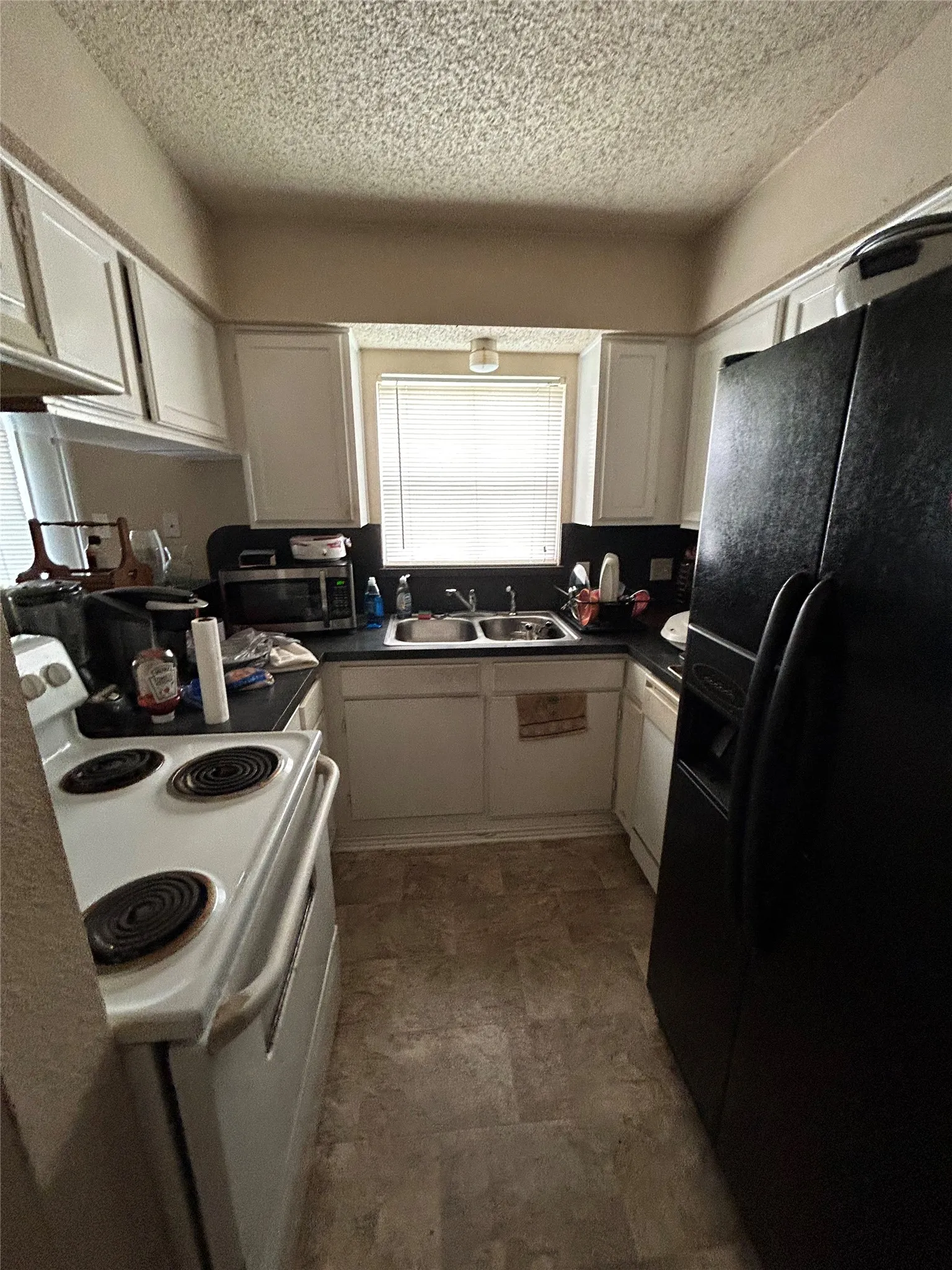 Kitchen featuring white cabinetry, dark countertops, a double basin sink, and a window with blinds