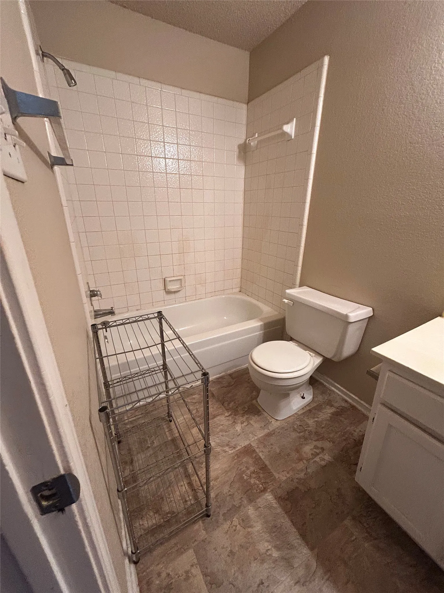 Bathroom featuring a white bathtub with subway tile surround, white toilet, and a white vanity with cabinet storage