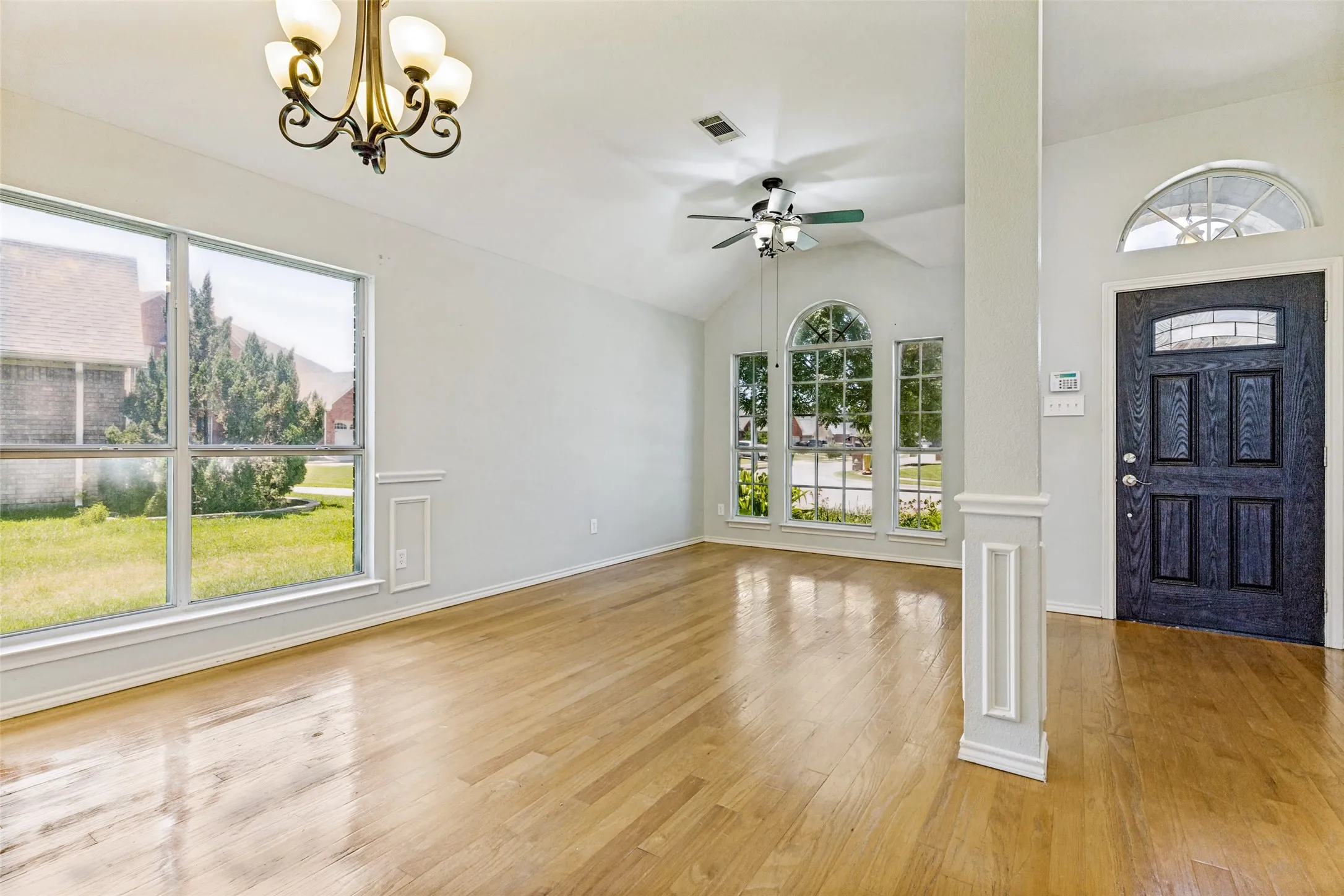 Spacious interior featuring wood-finish flooring, vaulted ceilings, and an elegant front entry door with an arched transom window