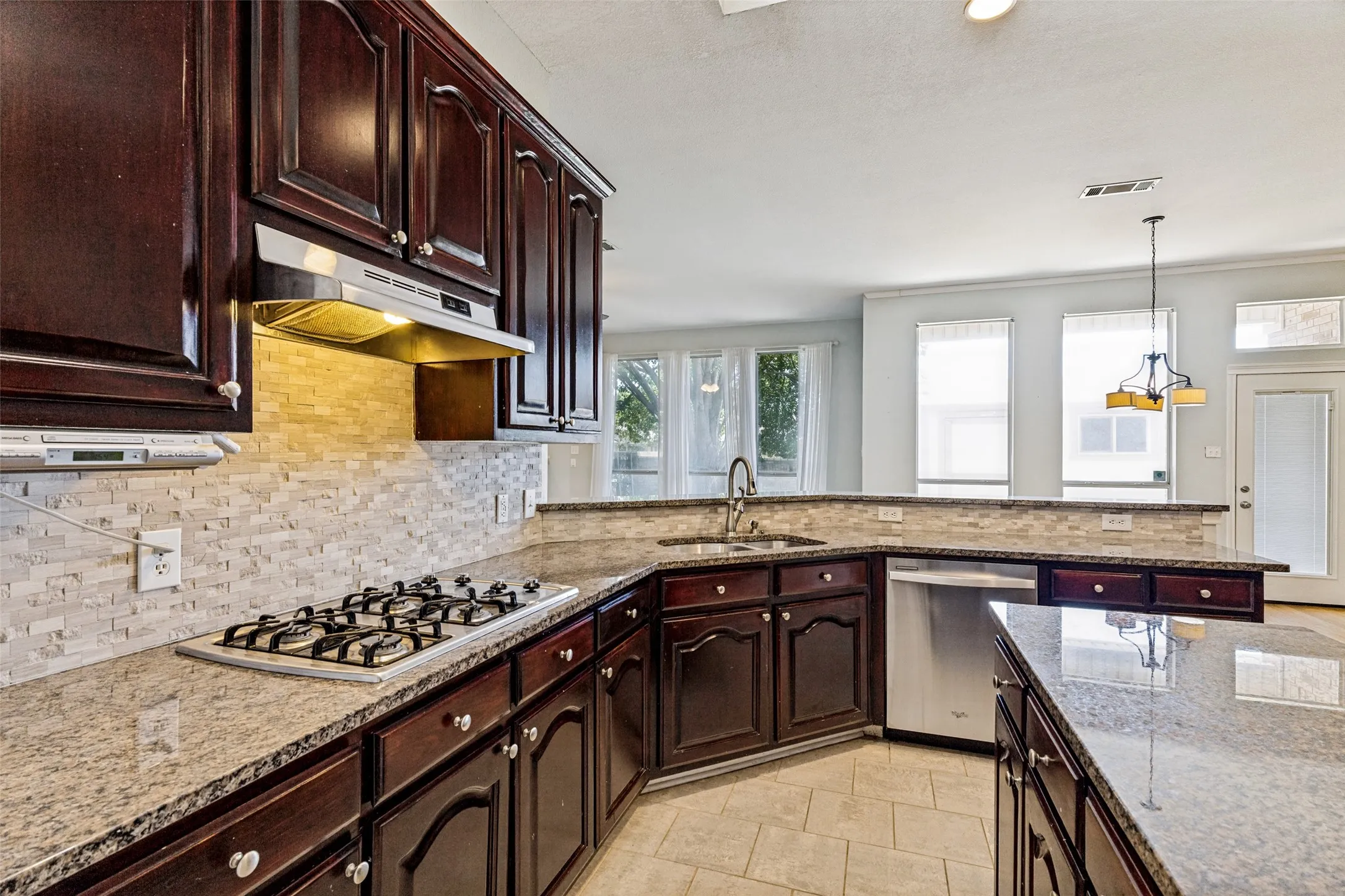 Kitchen featuring rich wood cabinetry, granite countertops, a tiled backsplash, built-in gas cooktop, and stainless steel dishwasher